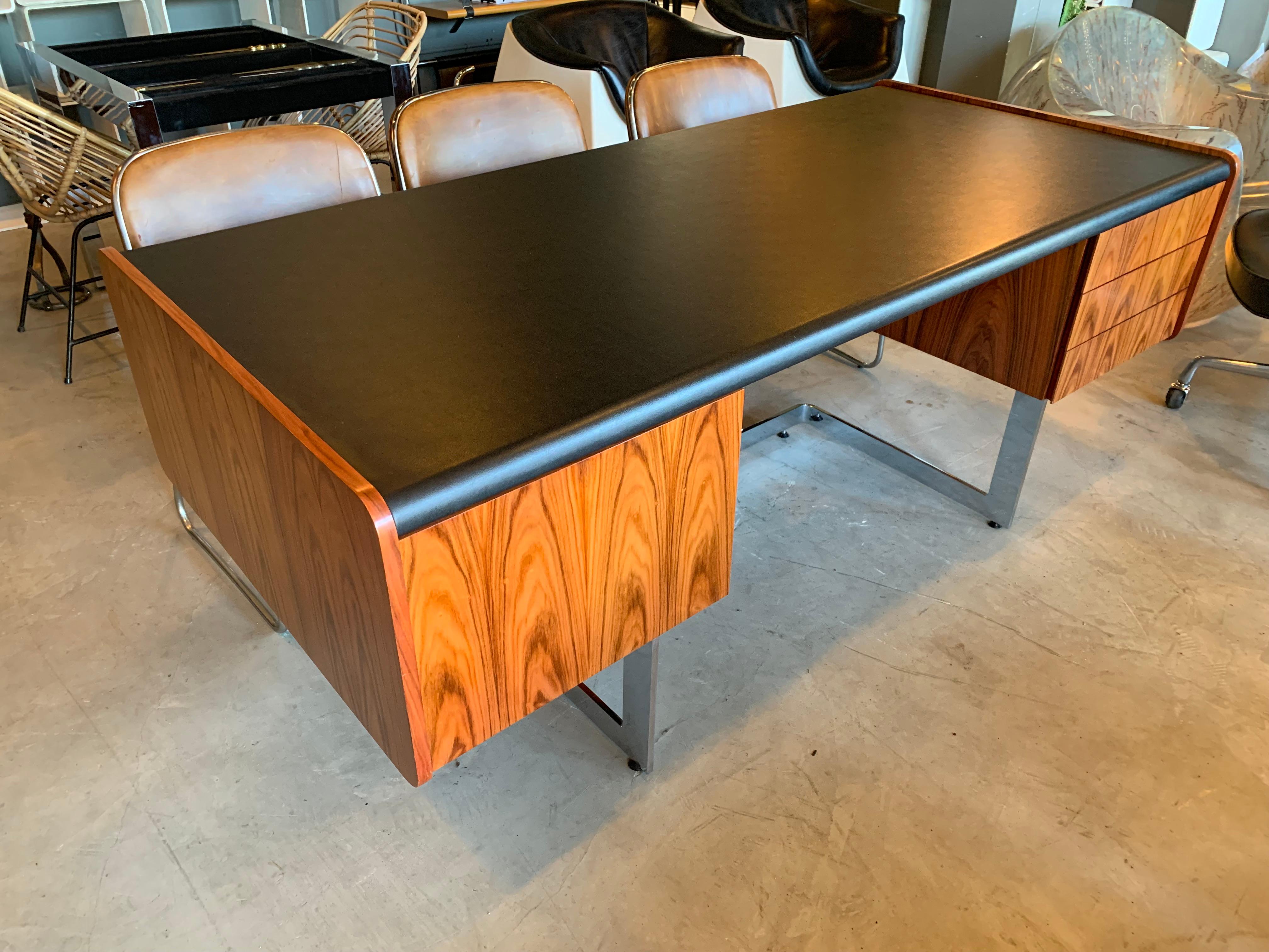 Stunning desk by Ste. Marie & Laurent. Floating rosewood desk with angular chrome base. Three drawers on right and functional file drawer with original/working lock on the left. Black vinyl top in perfect condition. Reflective chrome panel on back