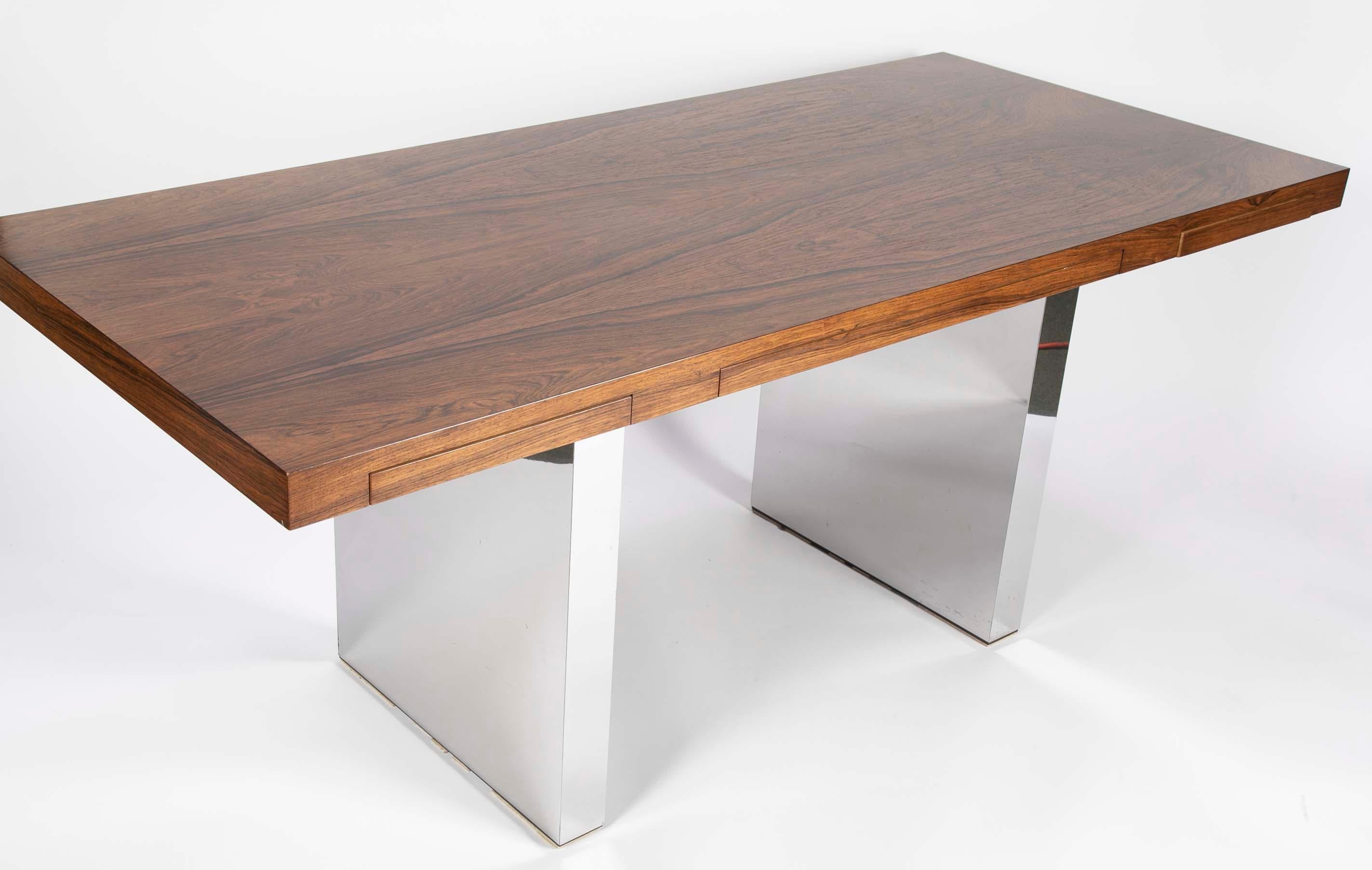A sleek rosewood desk with three minimal drawers that disappear into the apron. The drawers a constructed of white oak. A Dunbar metal tag is inside the left drawer. Chrome legs in perfect condition with no dents. Designed by Roger Sprunger in 1965.