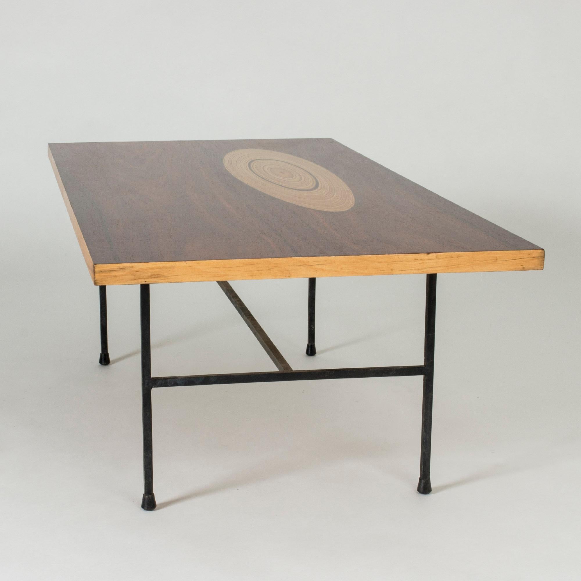 Stunning coffee table by Tapio Wirkkala, with a rosewood top inlayed with an oval shape of contrasting wood that has a growth ring-like pattern. Exquisitely restored. Sturdy base made from black lacquered metal.