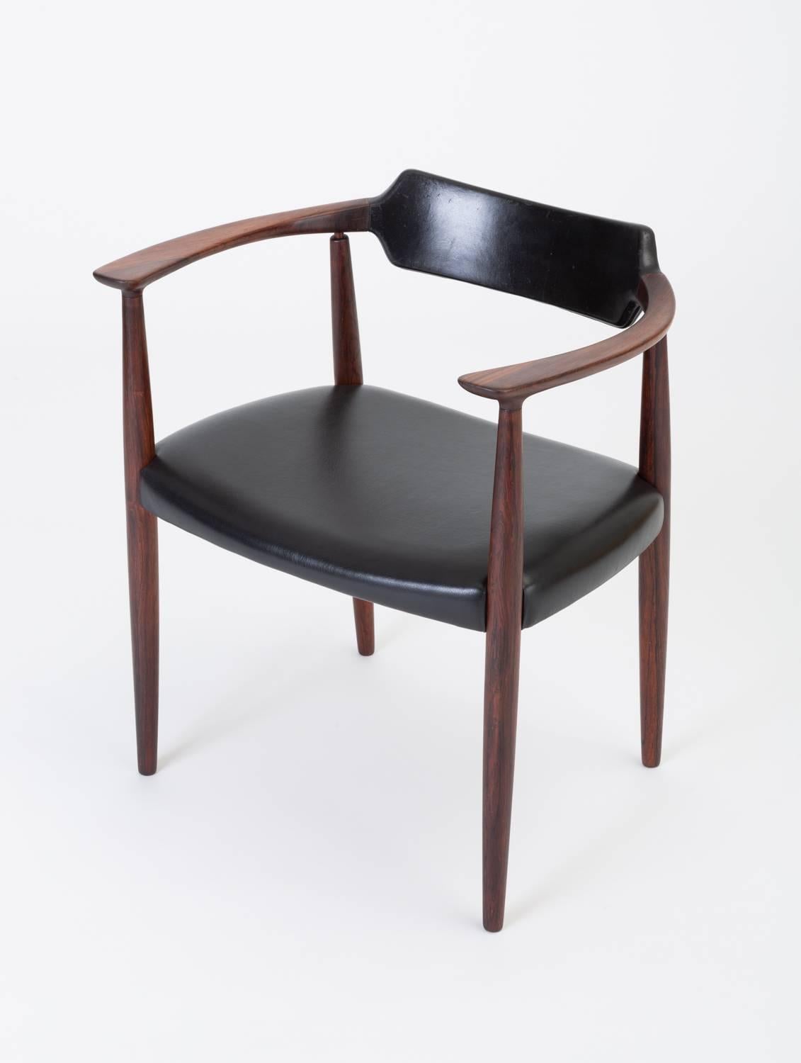 Designed in 1960 by Bent Andersen for Danish manufacturer Christensen & Larsen, this captain chair has a distinctive frame with high, flat arms that widens into a sculpted backrest, encased in patinated black leather. The wide seat is upholstered in