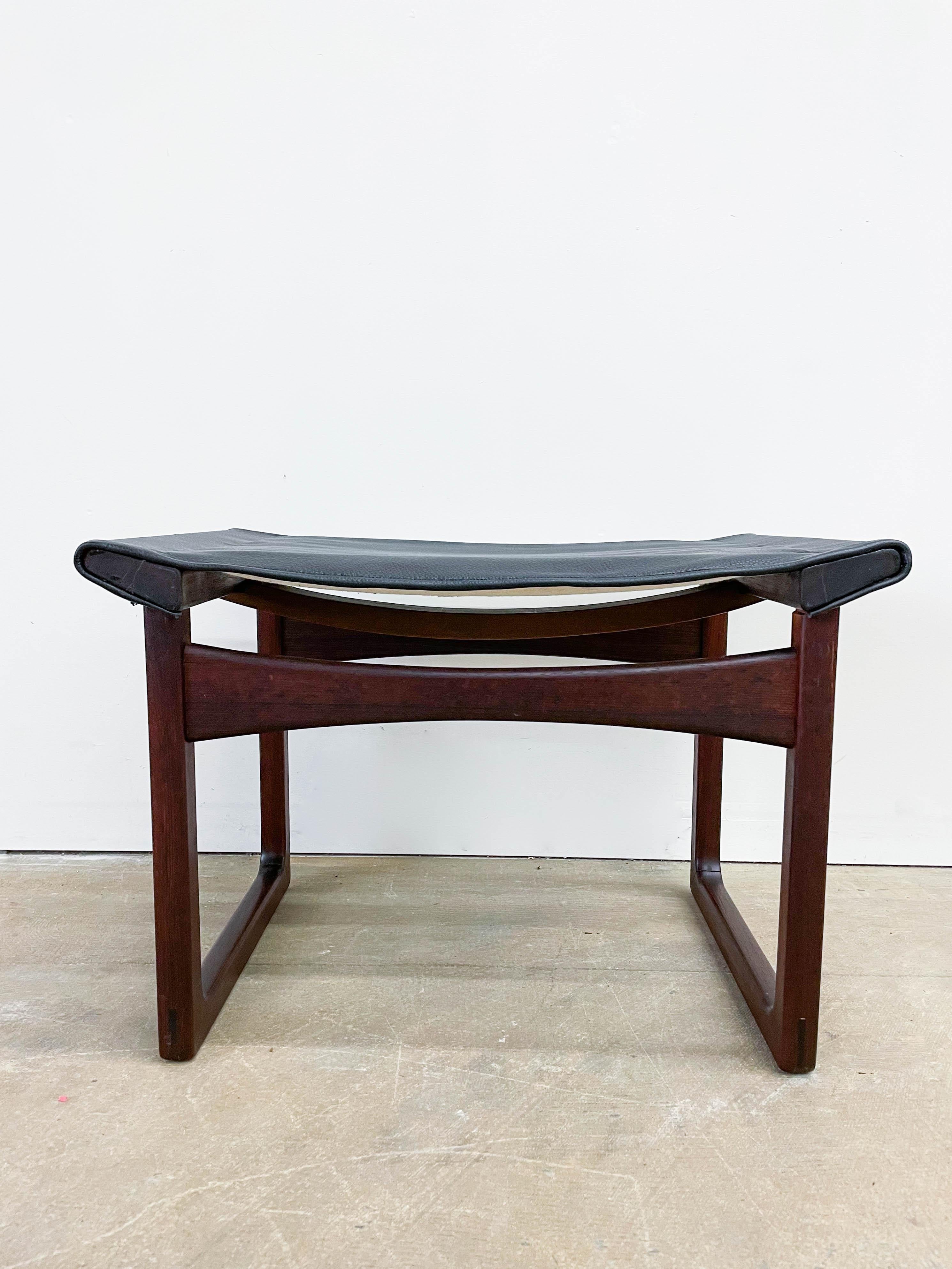 This is a beautiful Danish modern footstool designed by Aksel Bender Madsen and Ejner Larsen and made by Ludvig Pontopiddian in the late 1950s. The footstool boasts a solid rosewood frame with nice joinery detail such as through tennons on the