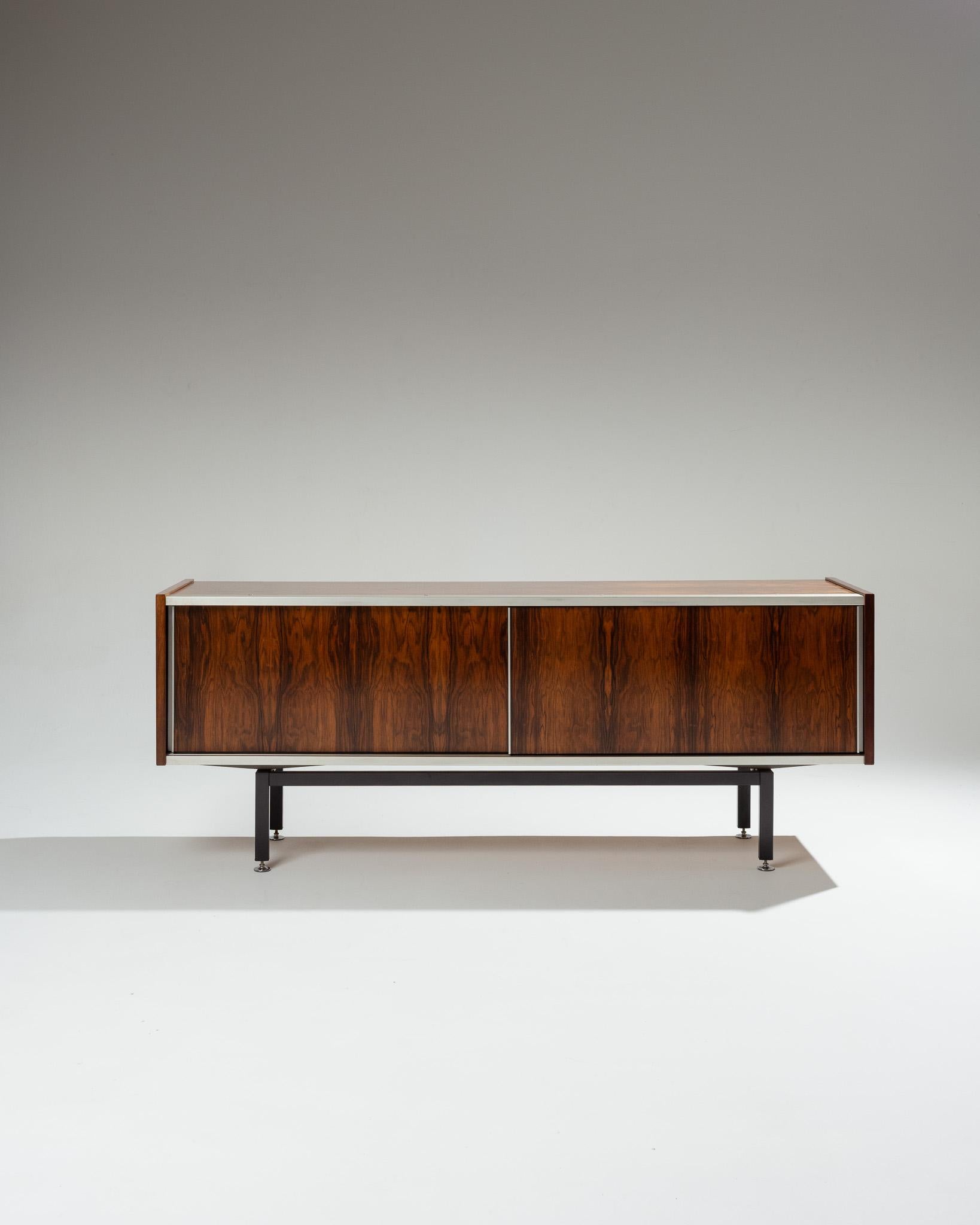 Enfilade edita da EFA, disegnata da Georges Frydman alla fine degli anni 1960. Struttura in legno di palissandro con finiture in alluminio, dotata di due porte scorrevoli per l'apertura di due scompartimenti con ante regolabili. Lo stile rispecchia