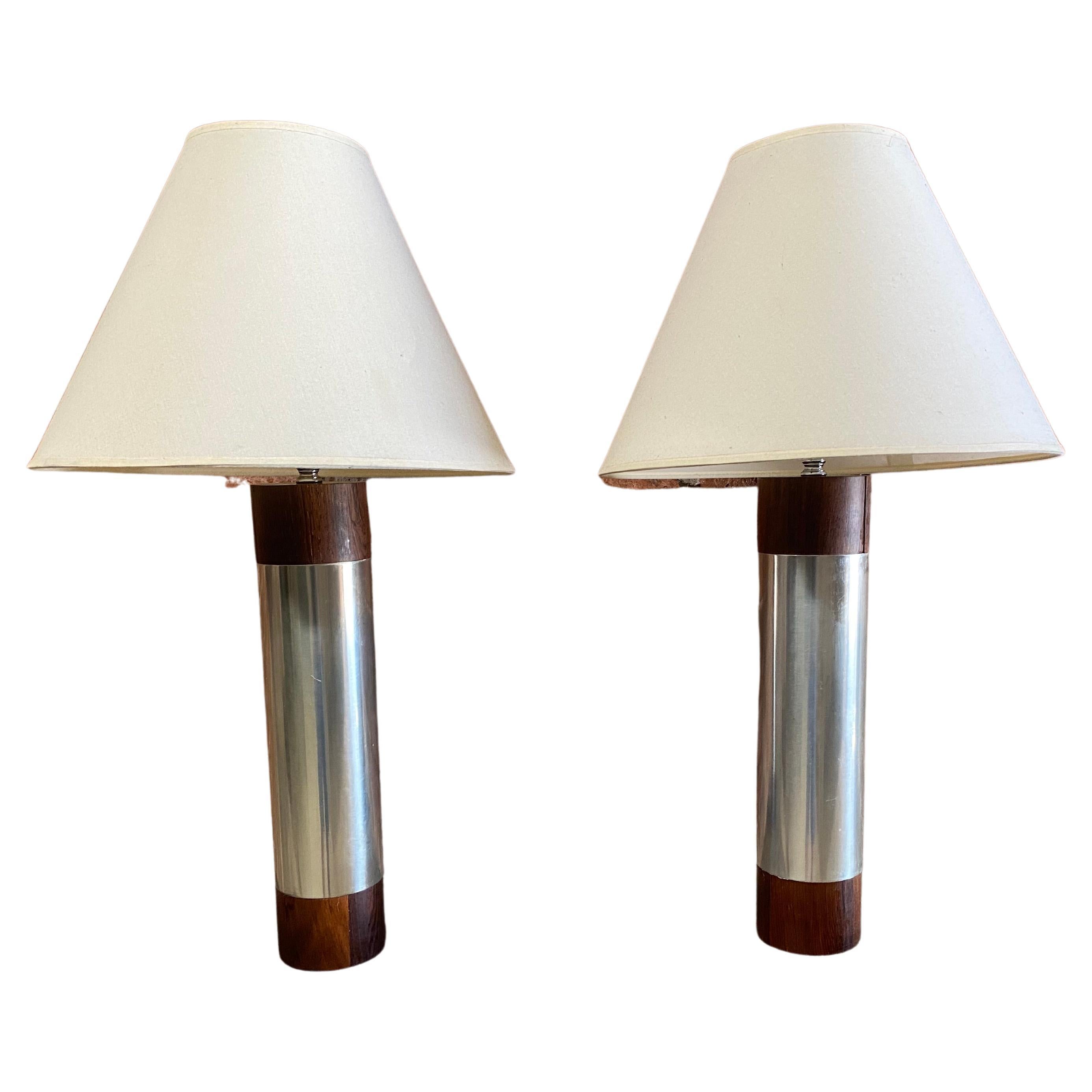 A fantastic pair of polished cylindrical aluminum and rosewood capped table lamps. Sleek and elegant design. Nicely figure rosewood grain complemented by the simple clean lines of the aluminum. They have a wonderful presence and will go just about