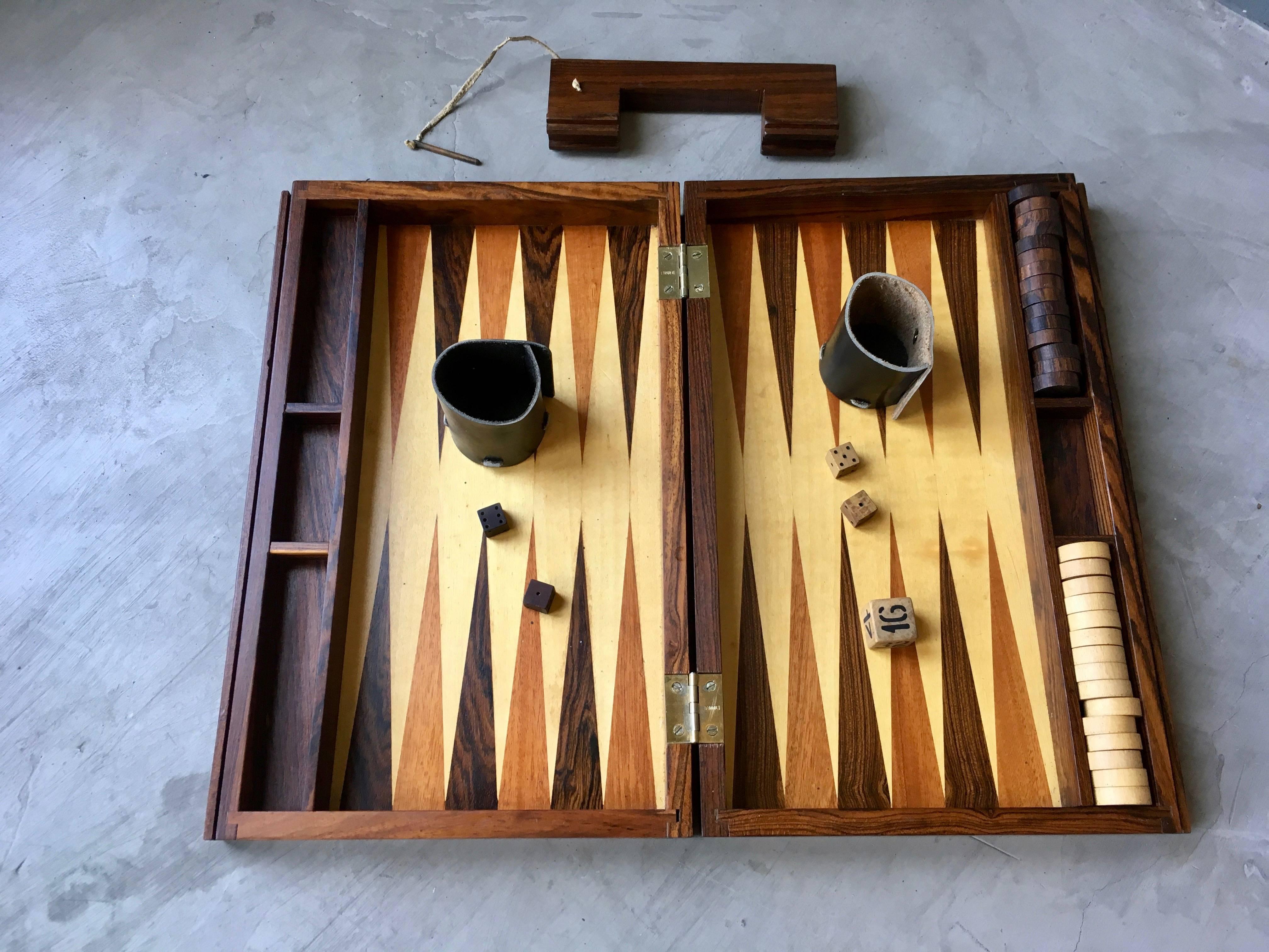 Stunning rosewood portable backgammon board. Handle slides out with inset brass pin. Board includes all pips, dice, leather cup holders and doubling cube. Gorgeous piece. Excellent condition.