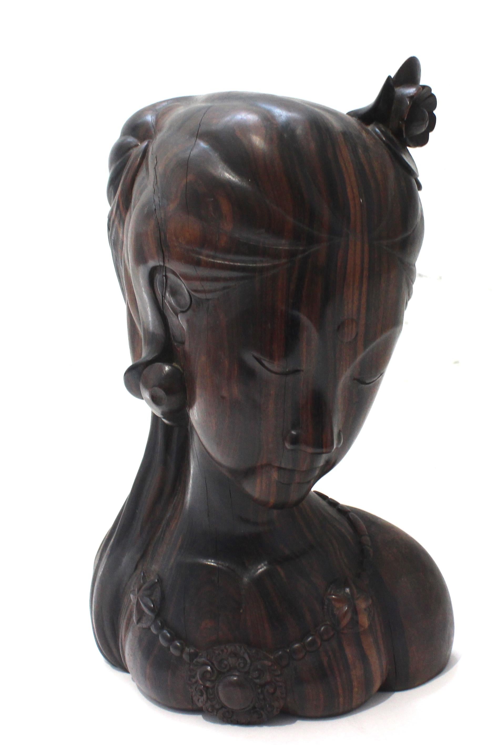 Cette élégante figurine en bois de rose représentant une jeune femme a été créée à Bali. Sa forme et l'utilisation des matériaux lui confèrent un caractère subtil. La figure est parée d'une seule fleur dans les cheveux, et d'un collier orné de