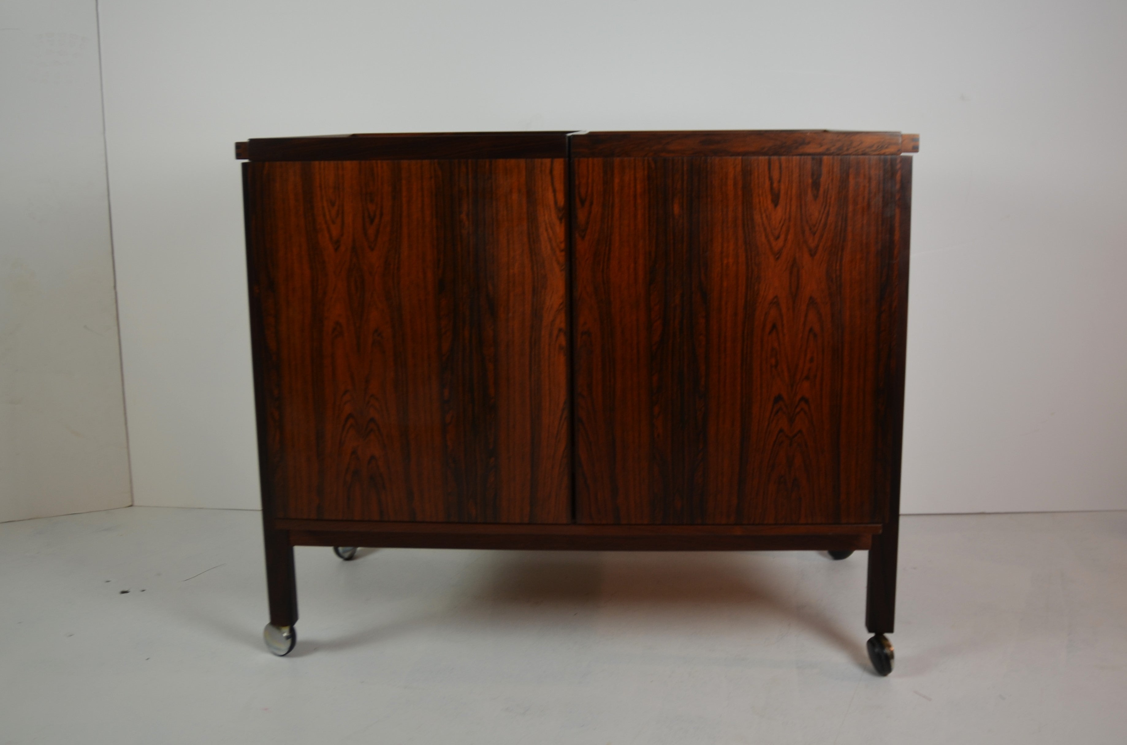 Mid-century rosewood bar cart by Erik Glasdam Jensen. Opens to reveal storage space and a black laminate top. Standing on four brass casters.