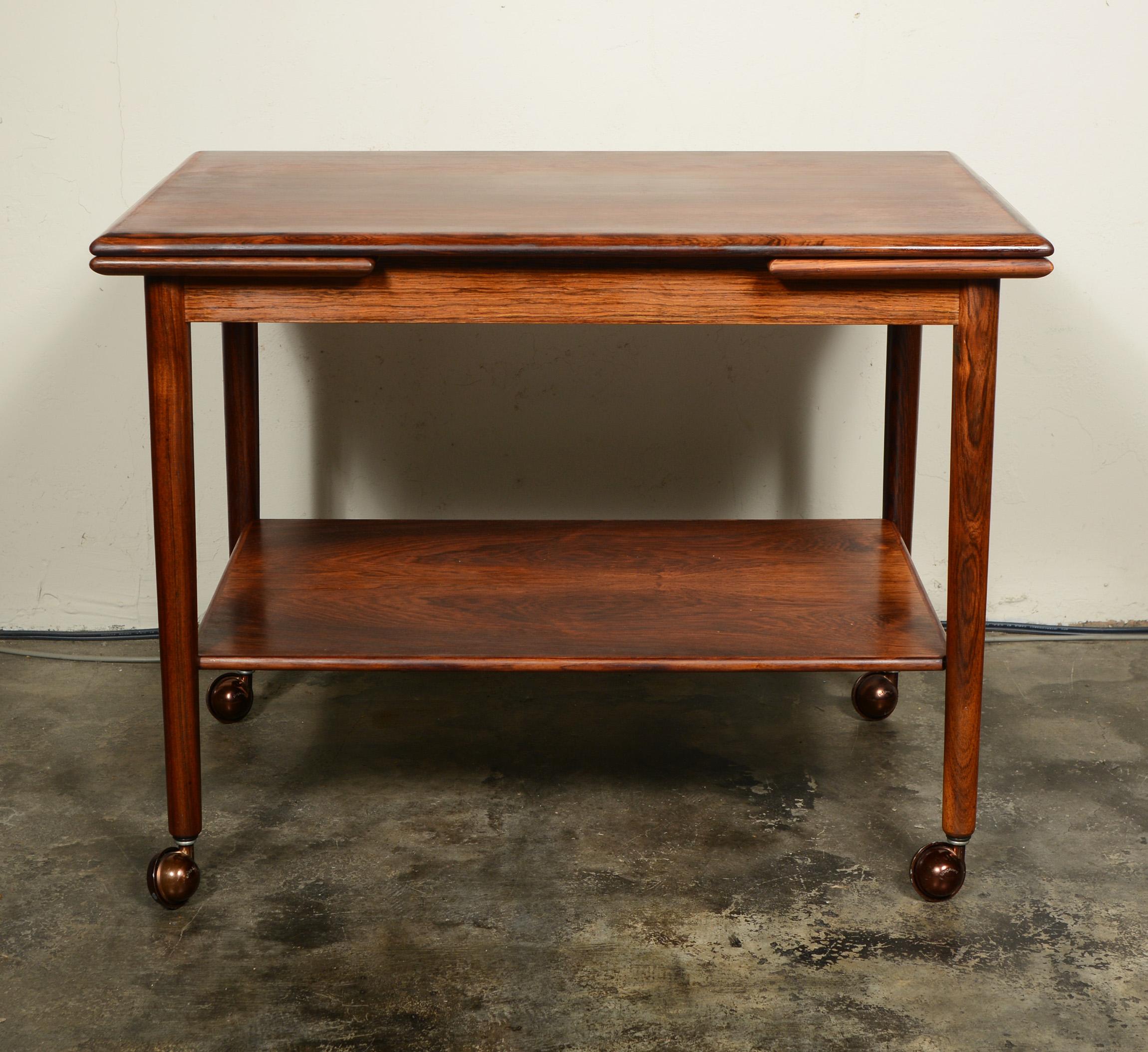 Danish rosewood bar cart made by M. H. Mobler. This cart has pull out leaves on the ends. One has a laminate inset to protect against spills and wet items. The cart has beautiful rich grain. The top and lower shelf have been refinished. The wheels