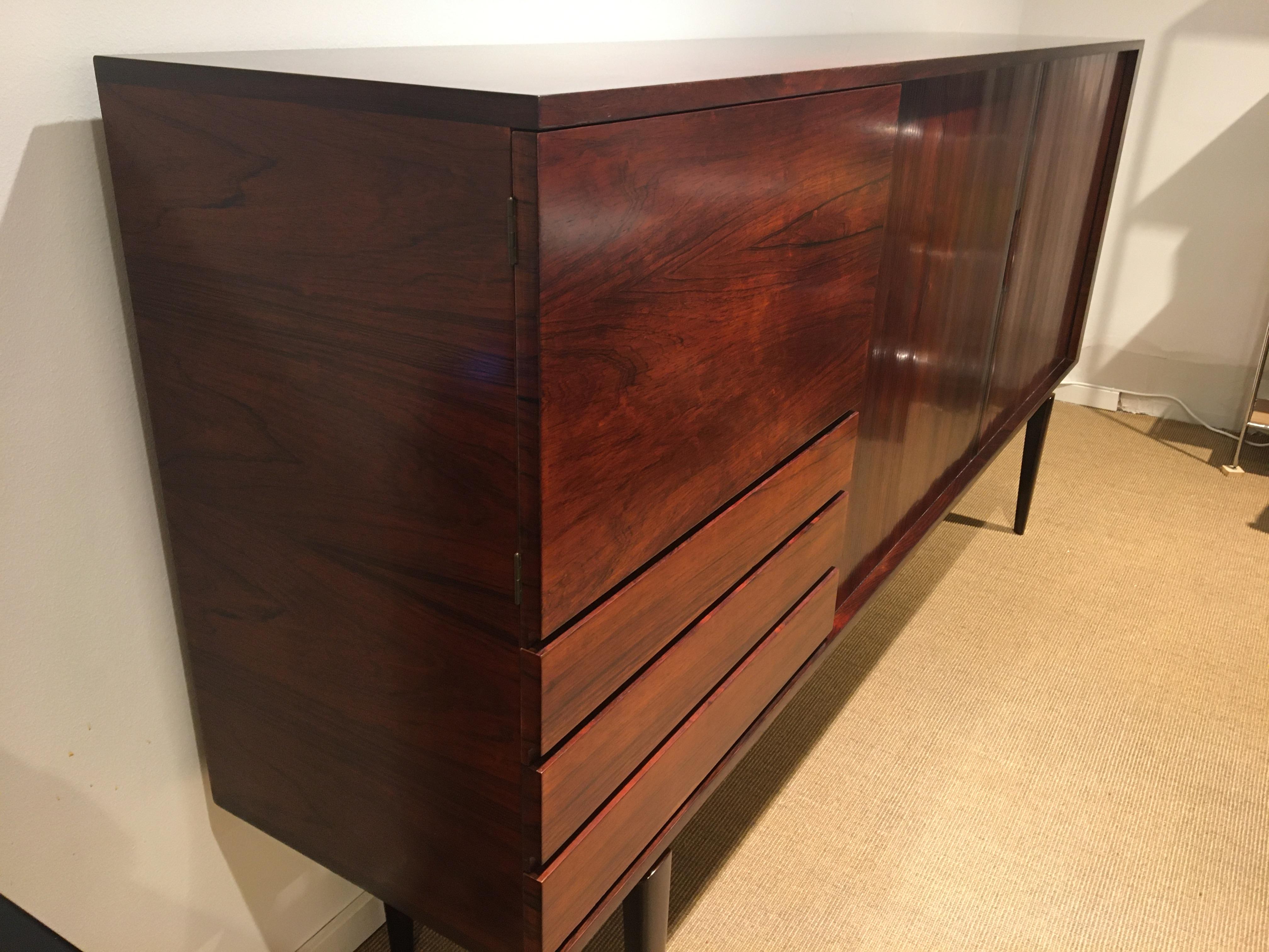 Rosewood High Sideboard newly restored. Design: H.W. Klein from Bramin Furniture.
The sideboard is made with hover.
Front with double blinds and milled handles, 1 large door and 3 drawers.
Inside the shutter doors are shelves in Oak.
Behind the door