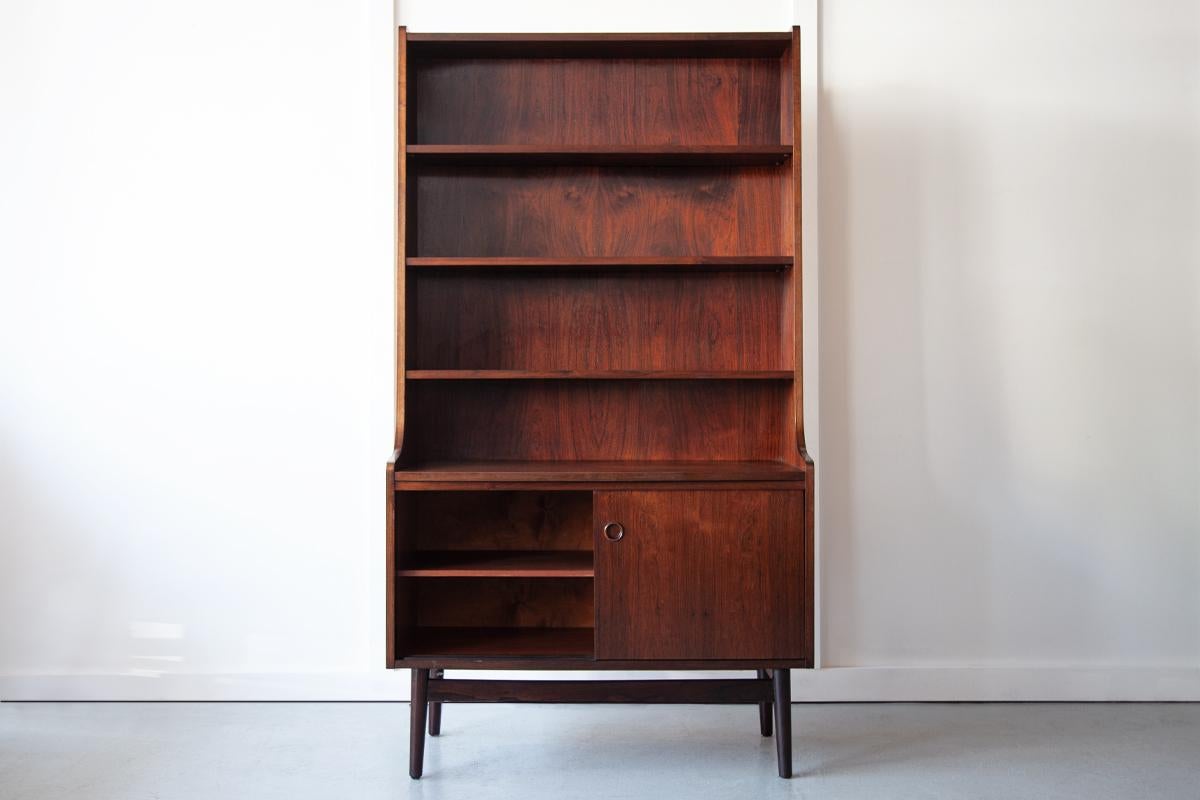 A beautiful Danish bookcase in rosewood, designed in the early 1960's by Johannes Sorth for Bornholm Mobelfabrik. These classic mid century units combine adjustable shelves and closed off cabinet storage beneath. The cabinet opens with sliding doors