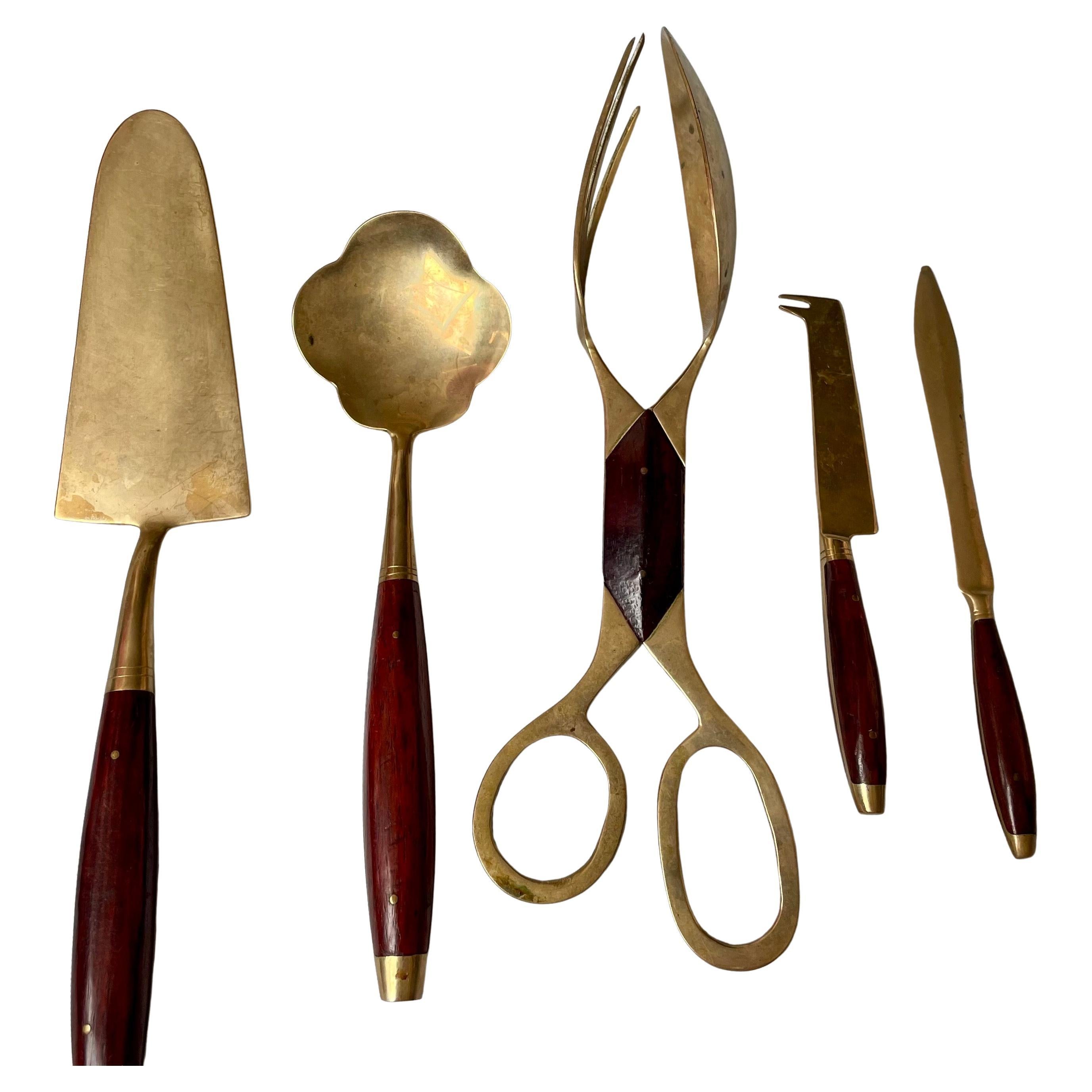 Voici un fantastique ensemble de 5 pièces de service en laiton avec des poignées en bois de rose. Les pinces ont un côté fourchette et un côté cuillère. Elles se détachent pour être utilisées séparément et mesurent 15 cm de long. Il y a une pelle à