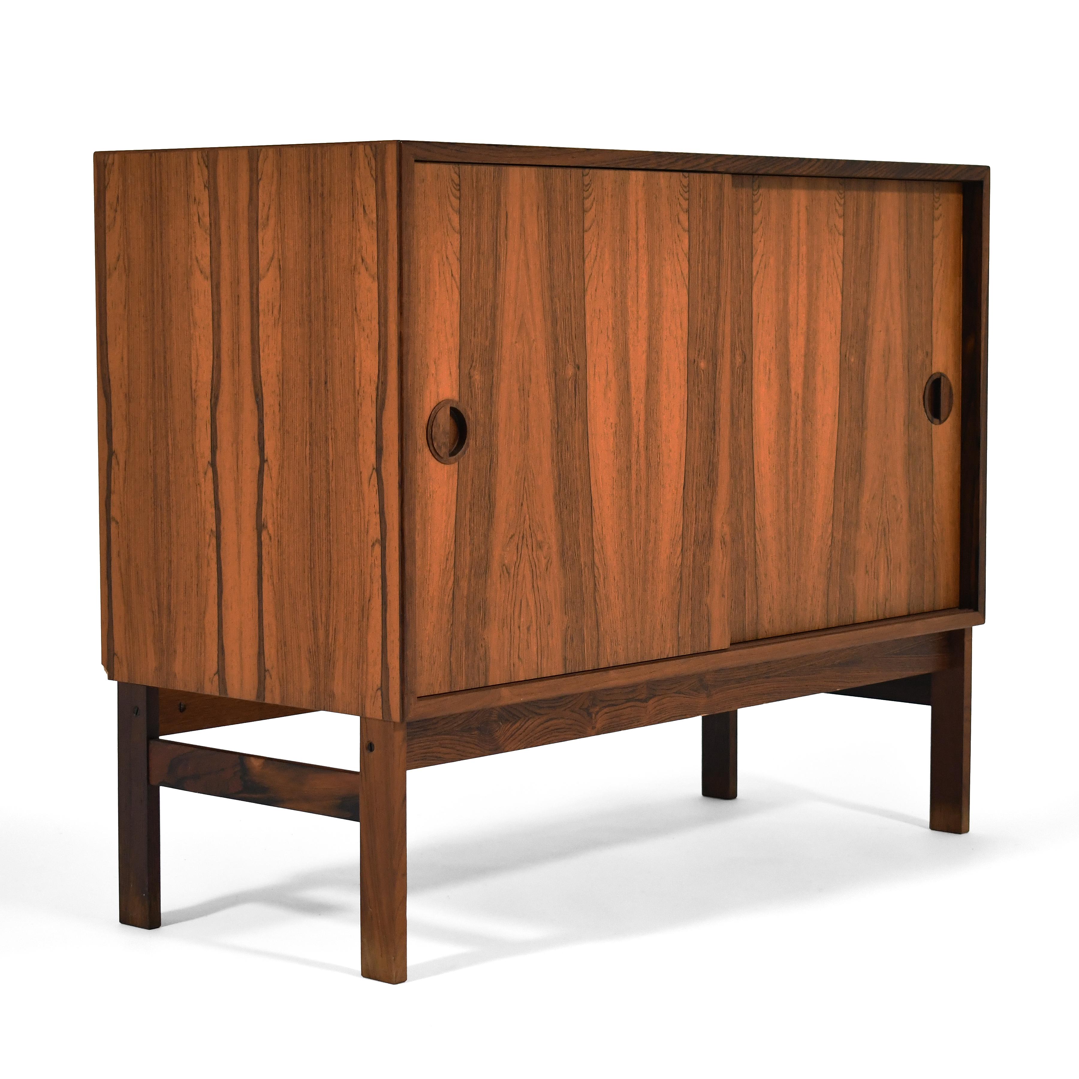 This beautiful cabinet was made in Denmark  by Hansen and Guldbord (HG Furniture). The clean-lined cabinet is clad in rosewood, and has round sculptural pulls on the sliding doors which conceal two cabinets- one with an adjustable shelf. The legs