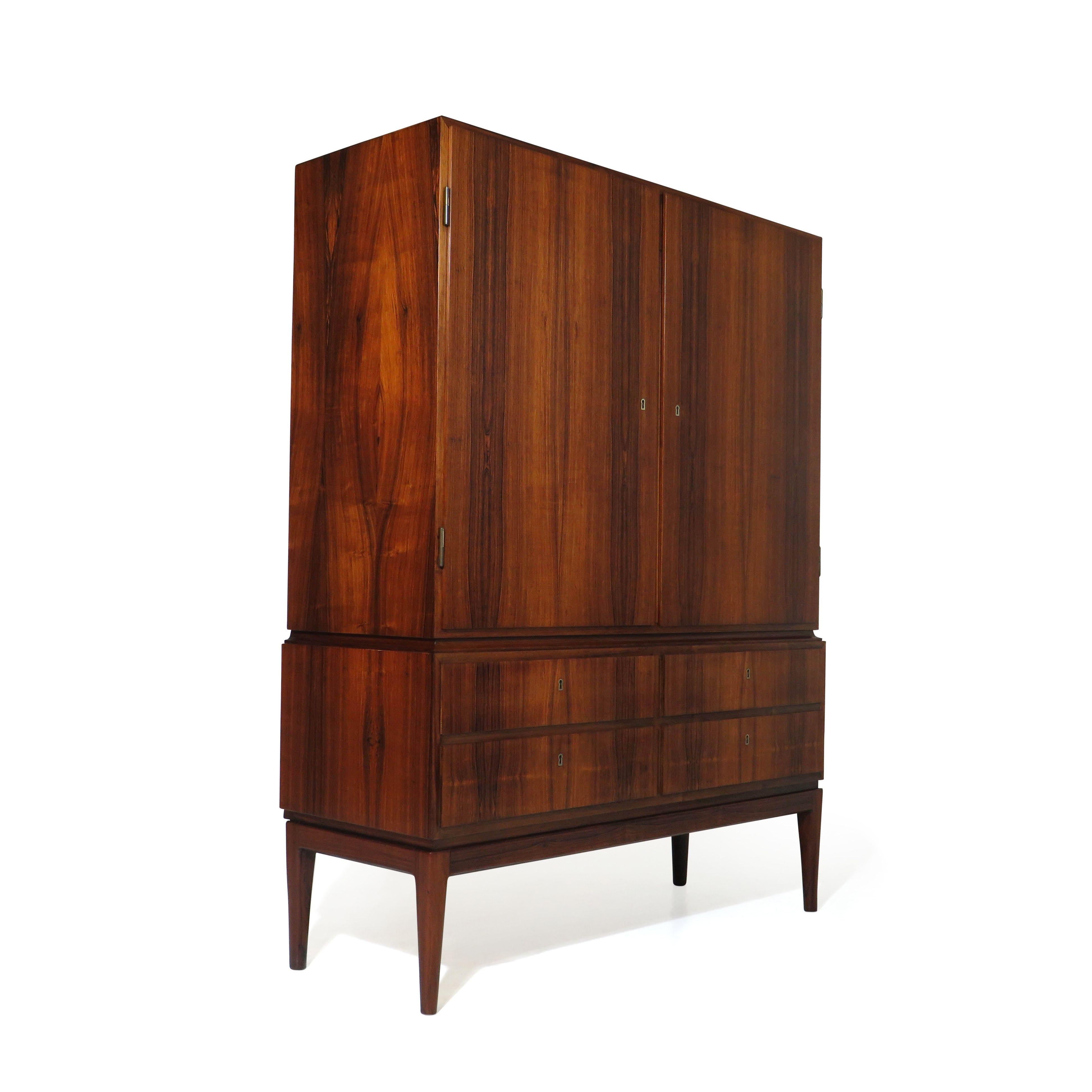Brazilian Rosewood sideboard cabinet, circa 1948, Denmark, with book-matched rosewood grain on two locking doors which open to reveal an interior of Cuban mahogany with adjustable shelves and three silverware or jewelry drawers, above four locking