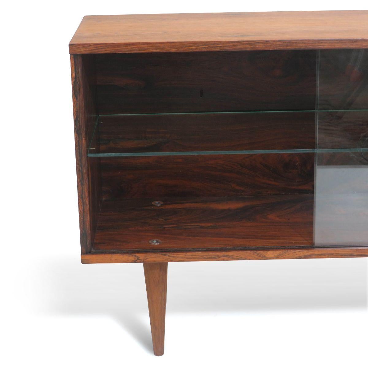 Mid-Century Modern rosewood cabinet, circa 1955 manufactured in Denmark. Crafted of rosewood with adjustable glass shelf and two glass sliding doors, raised on tapered legs. Modest proportions make for a versatile cabinet appropriate as a