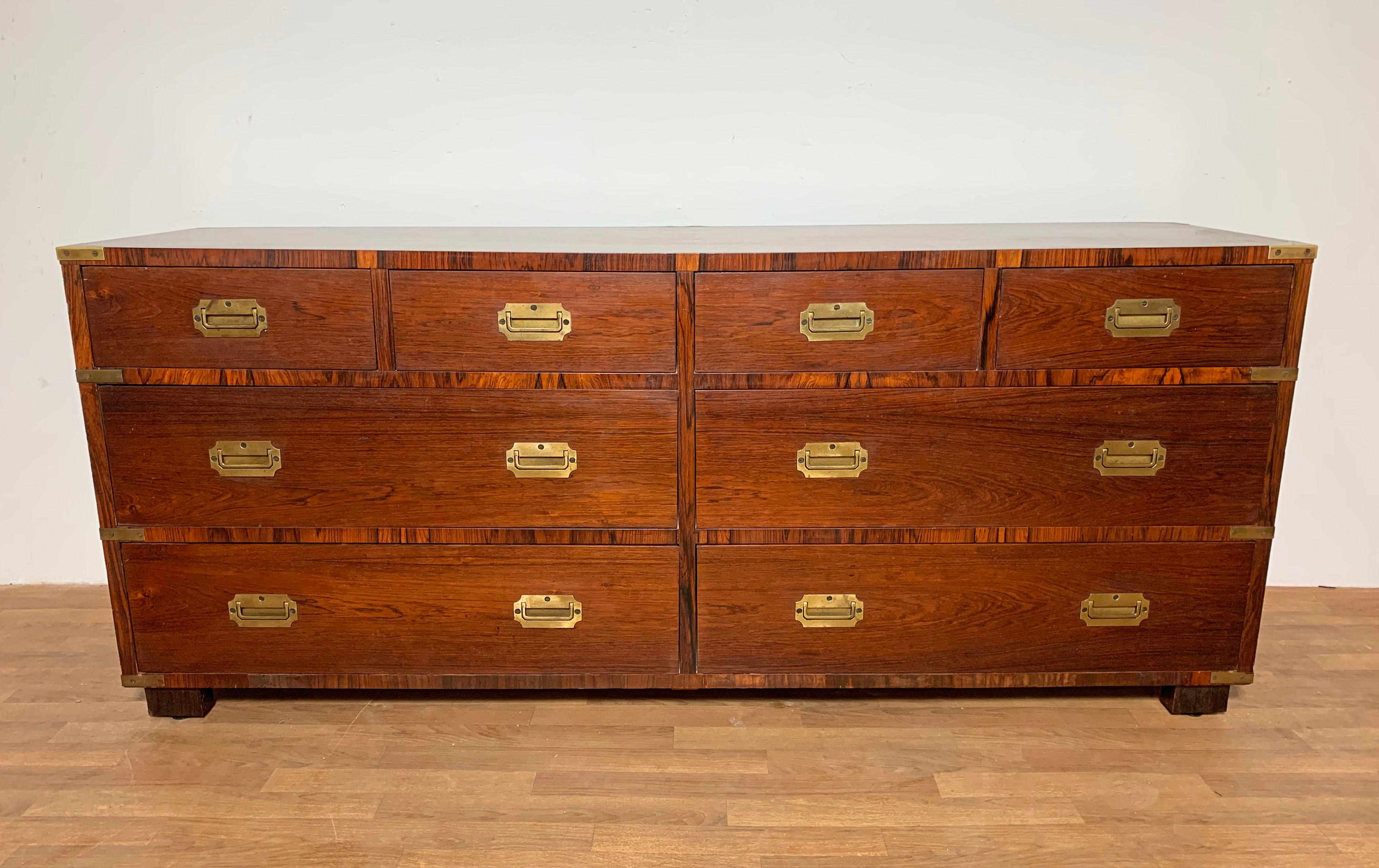 A high quality campaign style dresser in Brazilian rosewood of eight drawers with solid brass corner mounts and hardware, including lift handles. Made in England for the retailer John Stuart of New York in the 1950s.