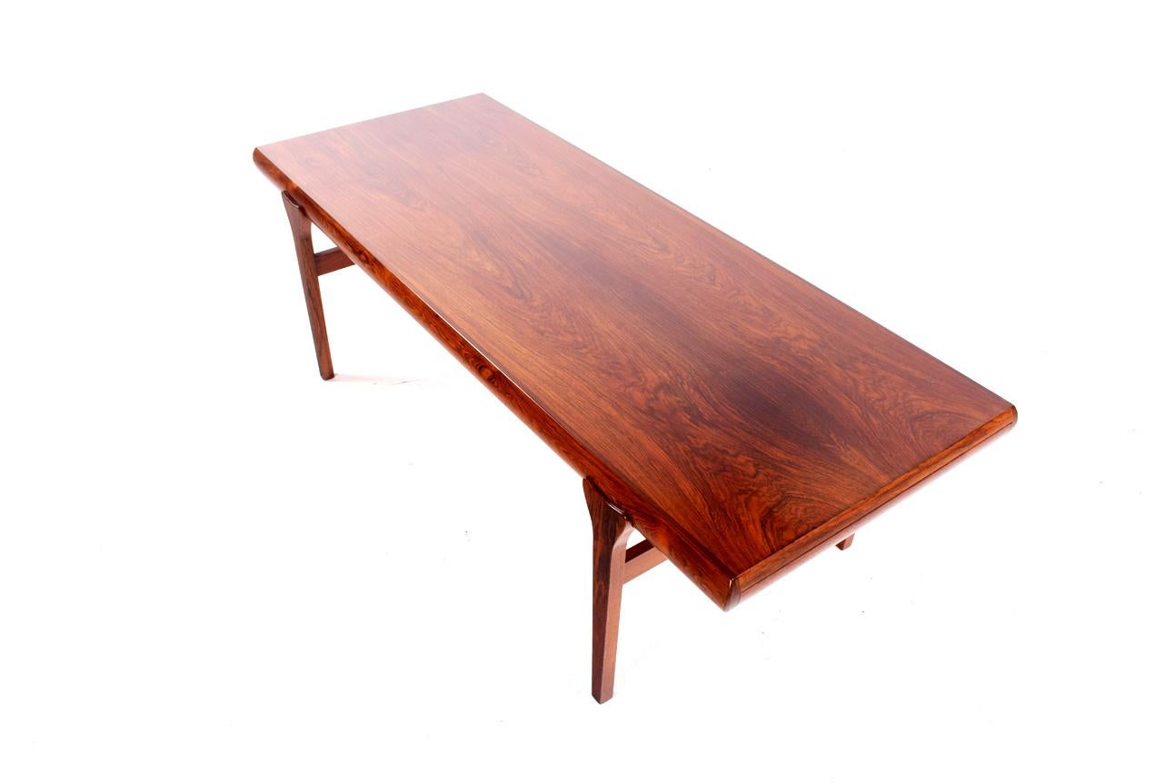 Authentic Mid-Century Modern rosewood coffee table designed by Johannes Andersen for C. F. Christensen. It features a lovely wood grain pattern, stylish sculpted legs, and a pull-out drawer and additional surface on either end!