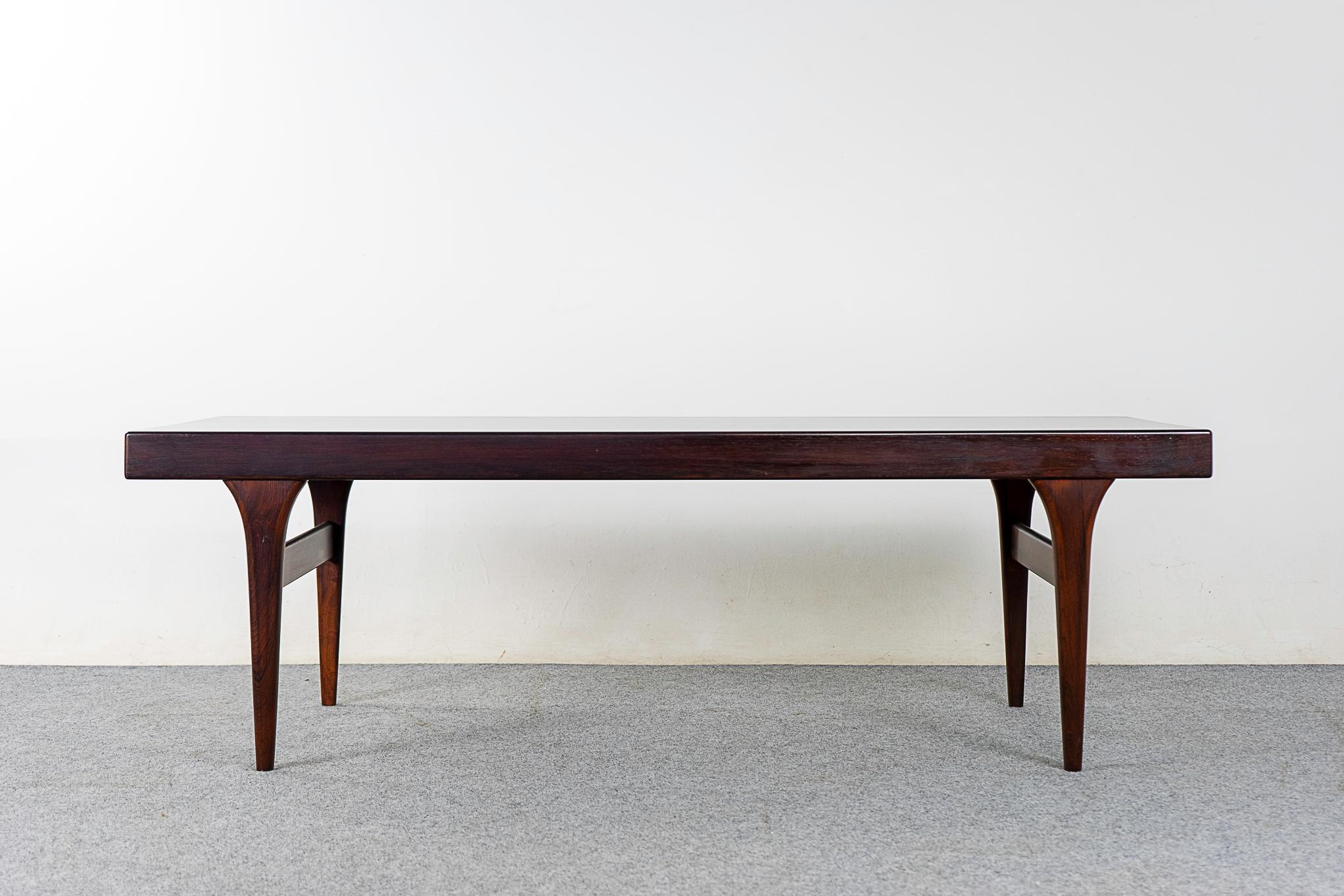 Rosewood mid-century Johannes Andersen coffee table, circa 1960's. Beautiful book matched veneer and solid wood edge along its length. Sculptural legs and cross supports. Each end has convenient integrated extenders, one teak and one black laminate