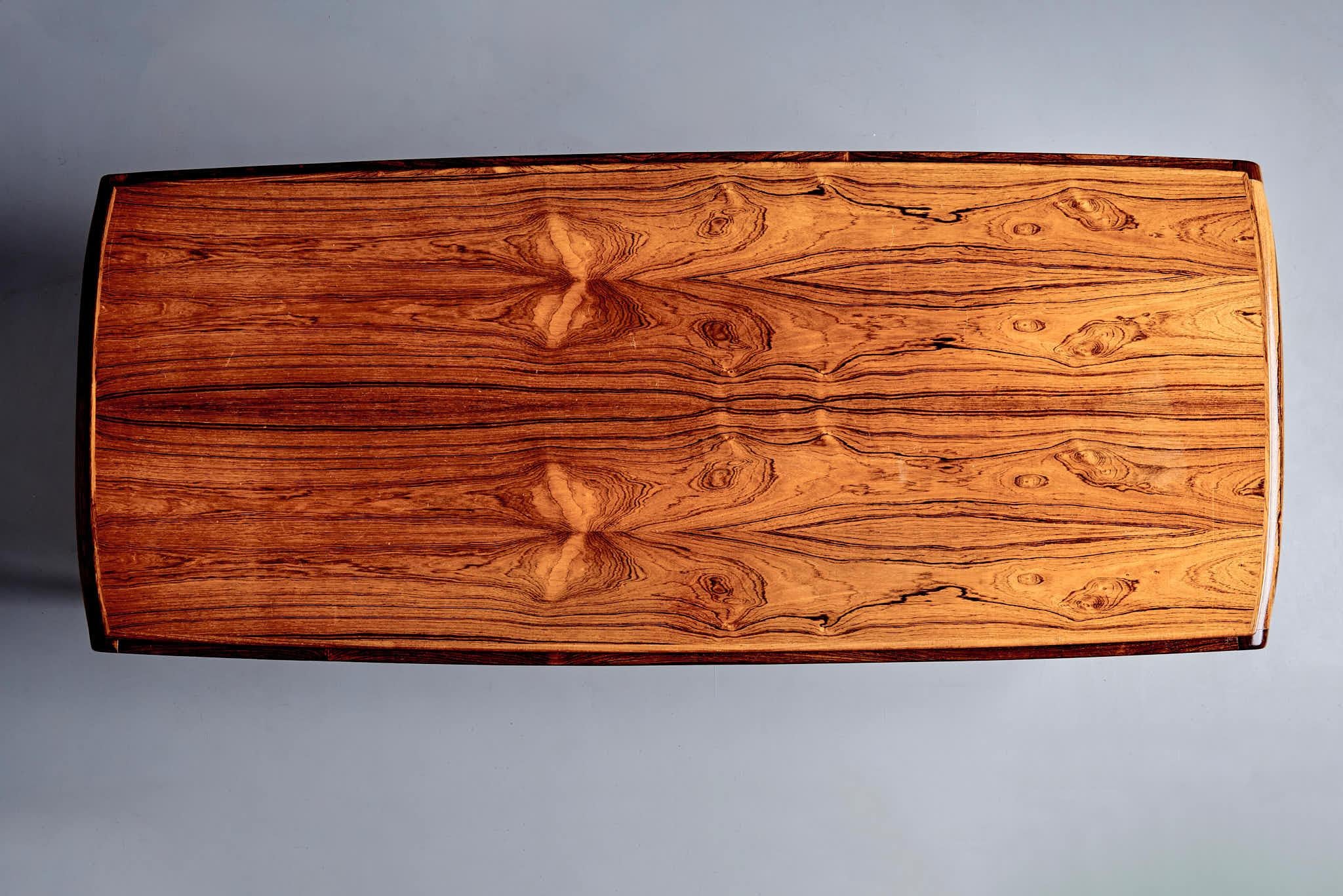 Tavolino rettangolare con piano impiallacciato in palissandro. Il piano presenta bellissimi motivi in legno naturale ed è rifinito con una laccatura lucida. La base è realizzata in legno di palissandro massiccio con supporti diagonali che