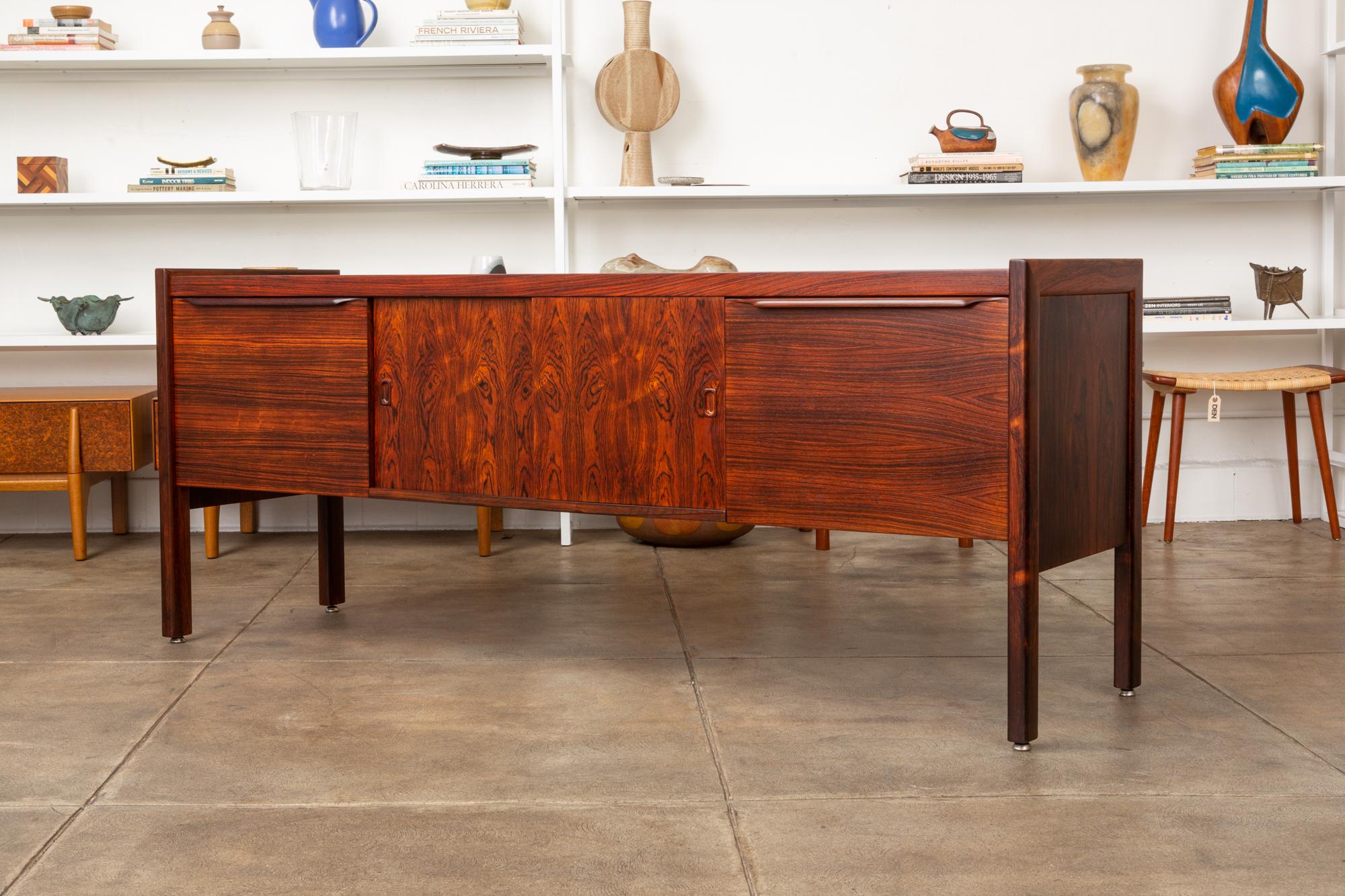 A stunning rosewood credenza, American, circa 1960s. The cabinet features a pair of highly figured rosewood sliding doors in the center of the piece with rosewood file drawers flanking either side. Both the doors and drawers have stylish sculpted