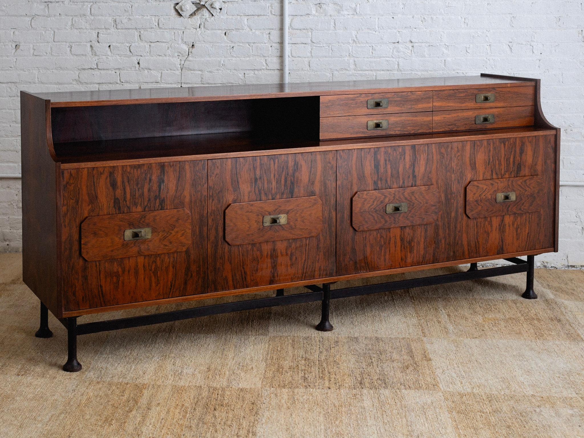 A mid century Brazilian style rosewood credenza. Credenza sits upon a sculpted iron base and features brass drawer pulls. Four doors open to reveal two cabinets, each with an inner shelf. Four petite upper drawers. Original unrestored finish.