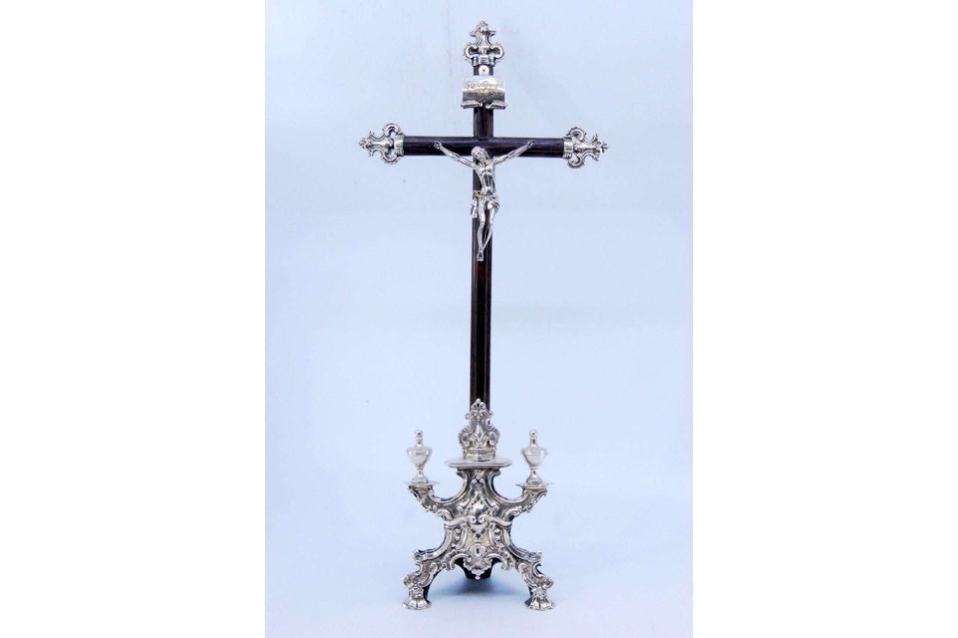 Description: Crucifix in rosewood with Jesus in silver, Christian symbols and resting on three feet. Metal: Silver. Origin: Portuguese. Mark: Absent. Weight: 308.35 grams. Dimensions: 38.5x16.5cm. Content: 900/1000. Assay Mark: Absent. Additional