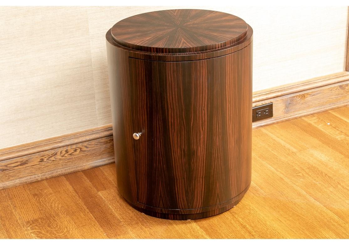 Meuble de bar ou table d'appoint cylindrique en palissandre avec une seule porte révélant une étagère de rangement. Le palissandre finement figuré forme un motif rayonnant frappant sur le plateau, qui est contrasté par les lignes verticales