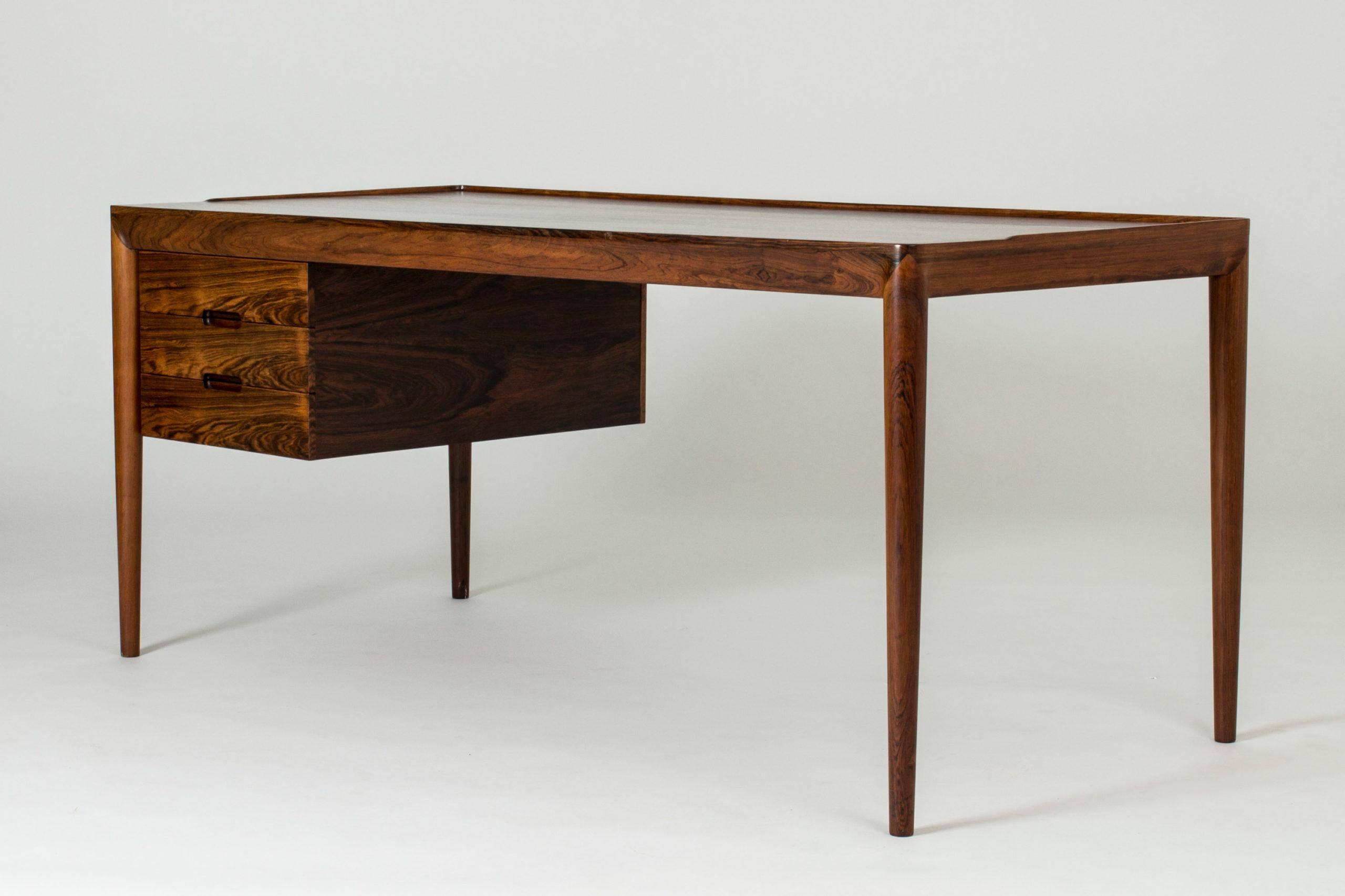 Rosewood desk by Erik Riisager Hansen in a very elegant and sleek design with nice details. Beautiful wood quality. The top drawer has a tray inside which can be pulled over the drawer and serve as a side extension.