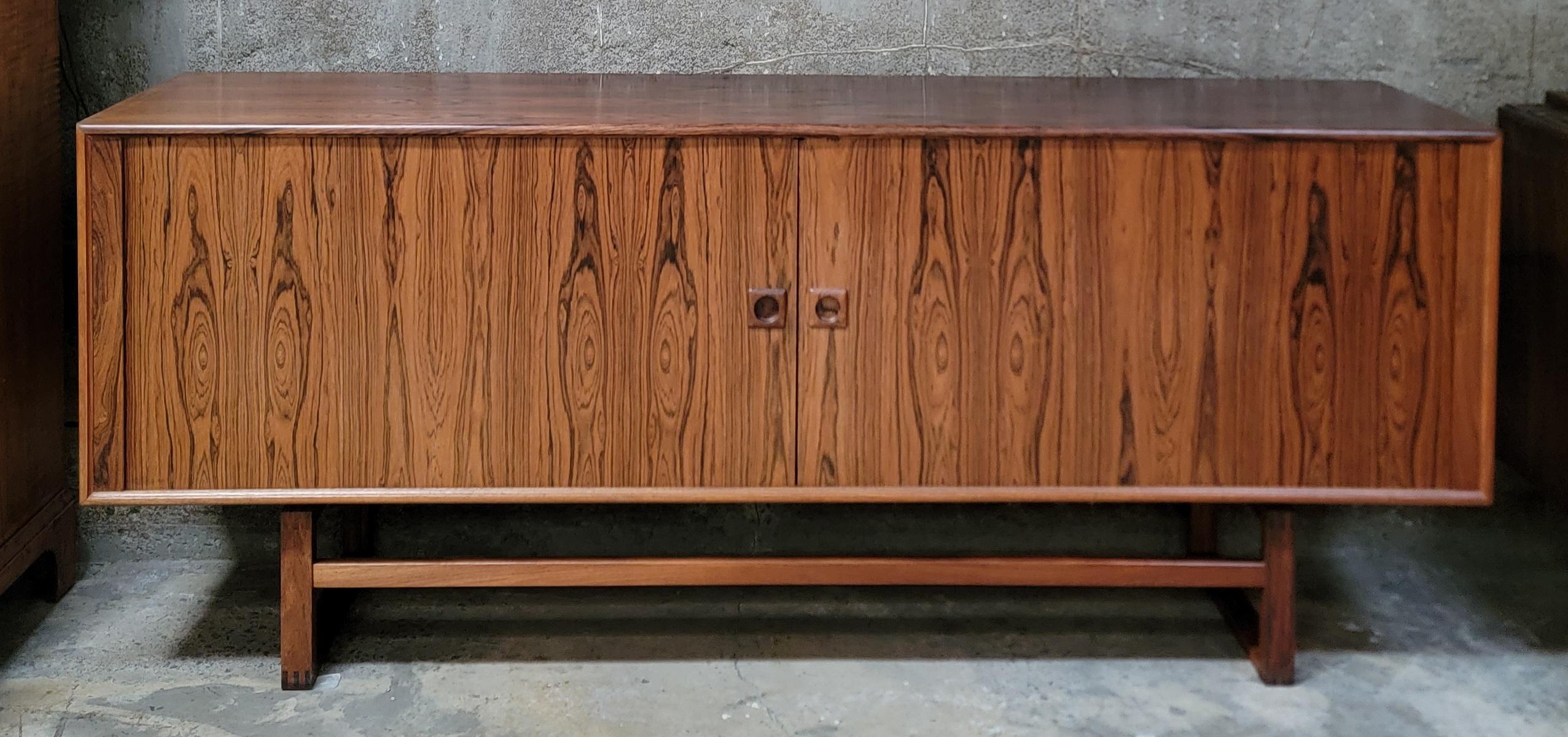 Bellissime venature del legno abbinate al libro in questa credenza lunga in legno di palissandro danese moderno degli anni '60. Le ante a tamburo si aprono su 3 cassetti interni e un ripiano regolabile. Finitura originale con un bel bagliore di