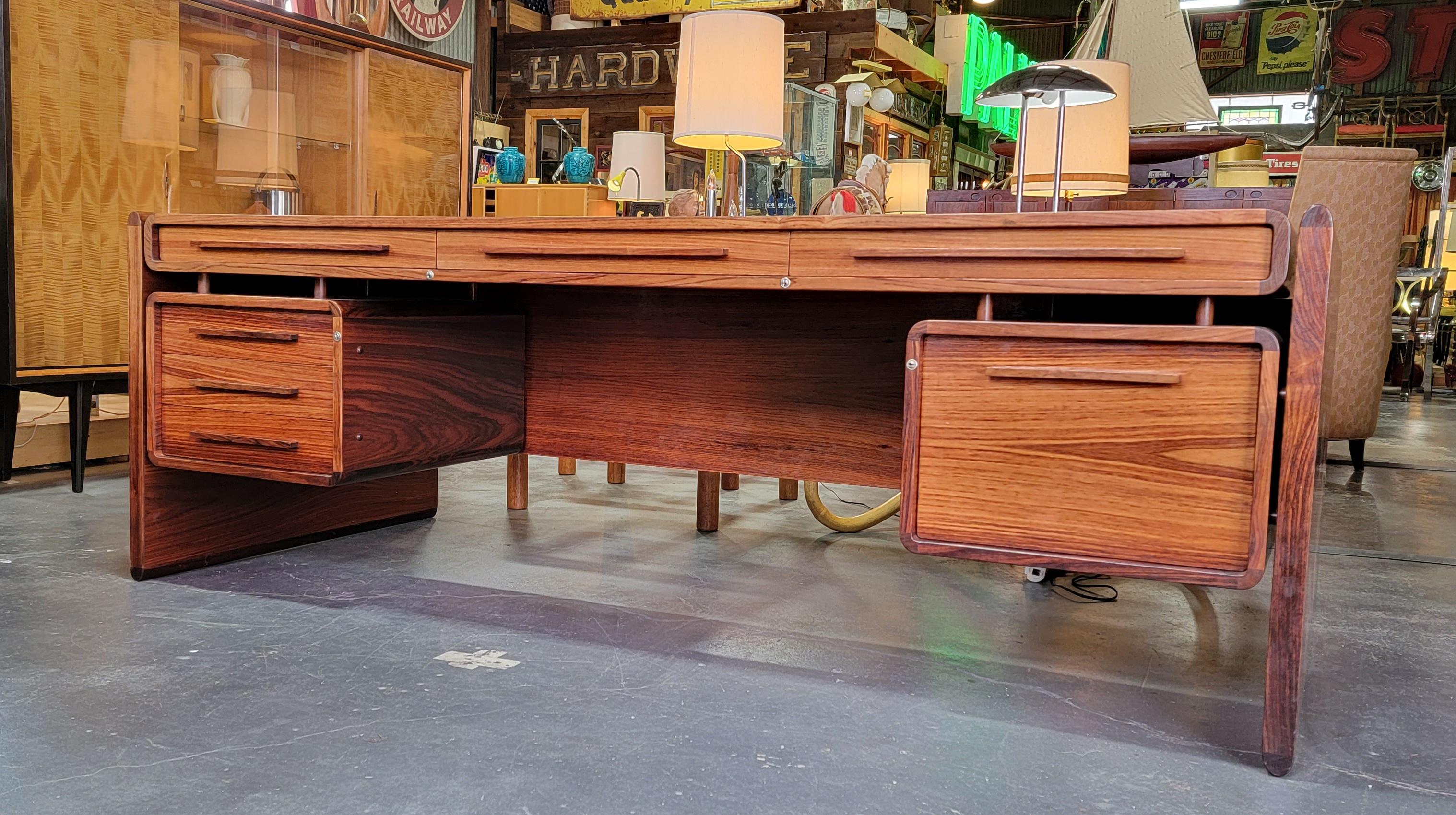 Impressive large-scale rosewood executive desk by Dyrlund Furniture of Denmark. Beautiful rosewood wood grain. Deep glow to original finish. Ample storage featuring a right hand file drawer, 3 upper drawers and 3 left hand drawers. Finished on all
