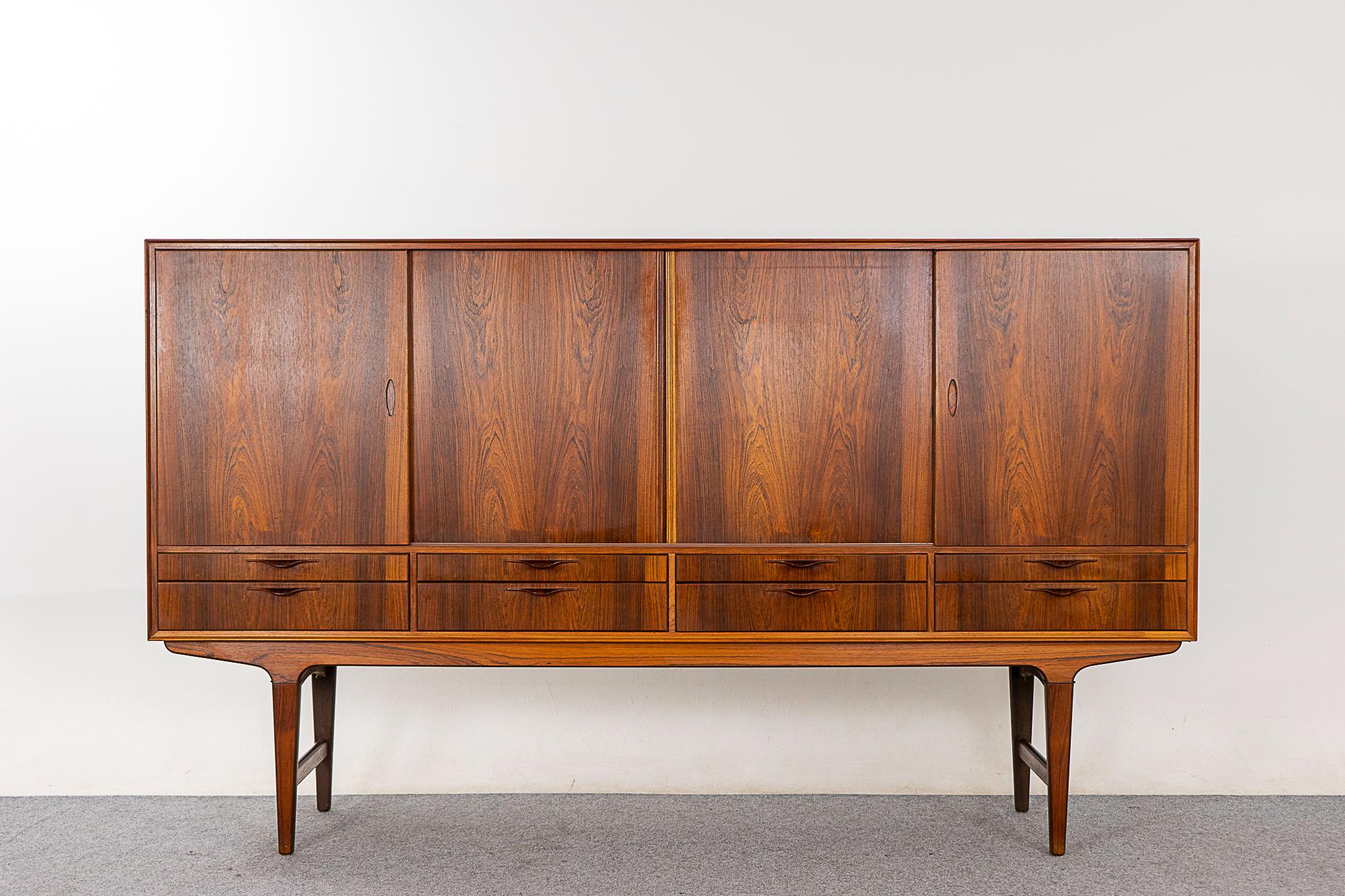 Rosewood mid-century sideboard, circa 1960's. Stunning grain patterns on the veneered case, doors and drawers. Angular base, lipped finger pulls, adjustable shelving, interior drawers and elegant cross supports. Storage for days, with style!