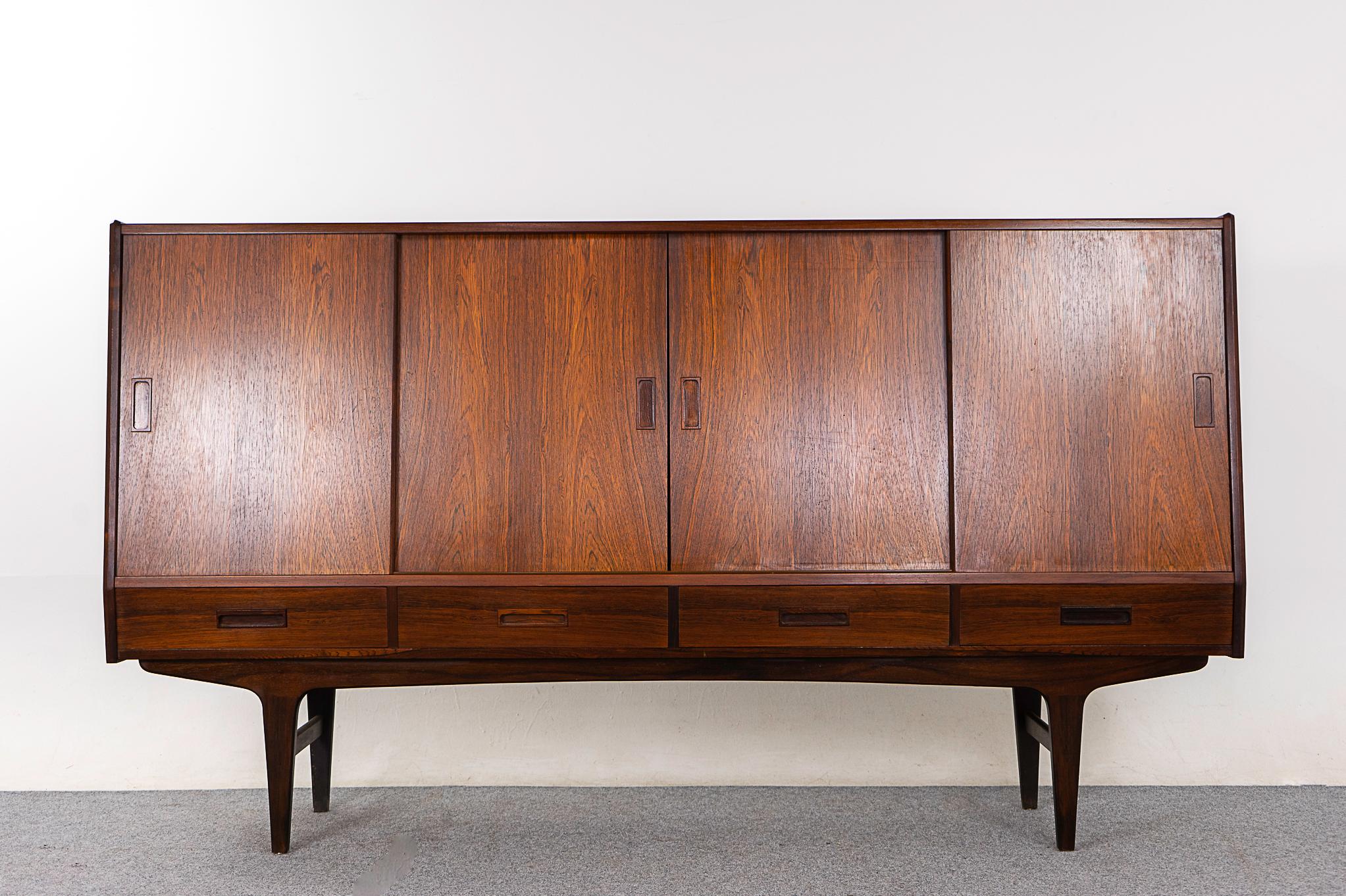 Rosewood mid-century sideboard, circa 1960's. Stunning veneered top and door faces. Unique angled front profile and interior bays with adjustable shelving, an etched mirrored bar and sleek felt lined drawers. Sculptural base with robust cross bars,