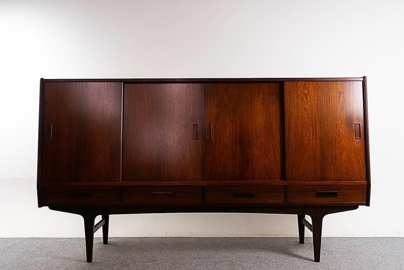 Rosewood mid-century sideboard, circa 1960's. Stunning veneered top and door faces. Unique angled front profile and interior bays with adjustable shelving, an etched mirrored bar and sleek felt lined drawers. Sculptural base with robust cross bars,