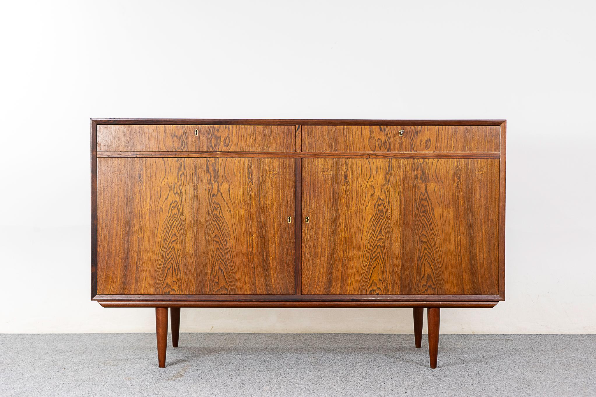 Rosewood mid-century sideboard, circa 1960's. Clean, simple design with exceptional book-matched veneer throughout. Locking doors and drawers, adjustable interior shelving and elegant tapering legs! 

Unrestored item with option to purchase in
