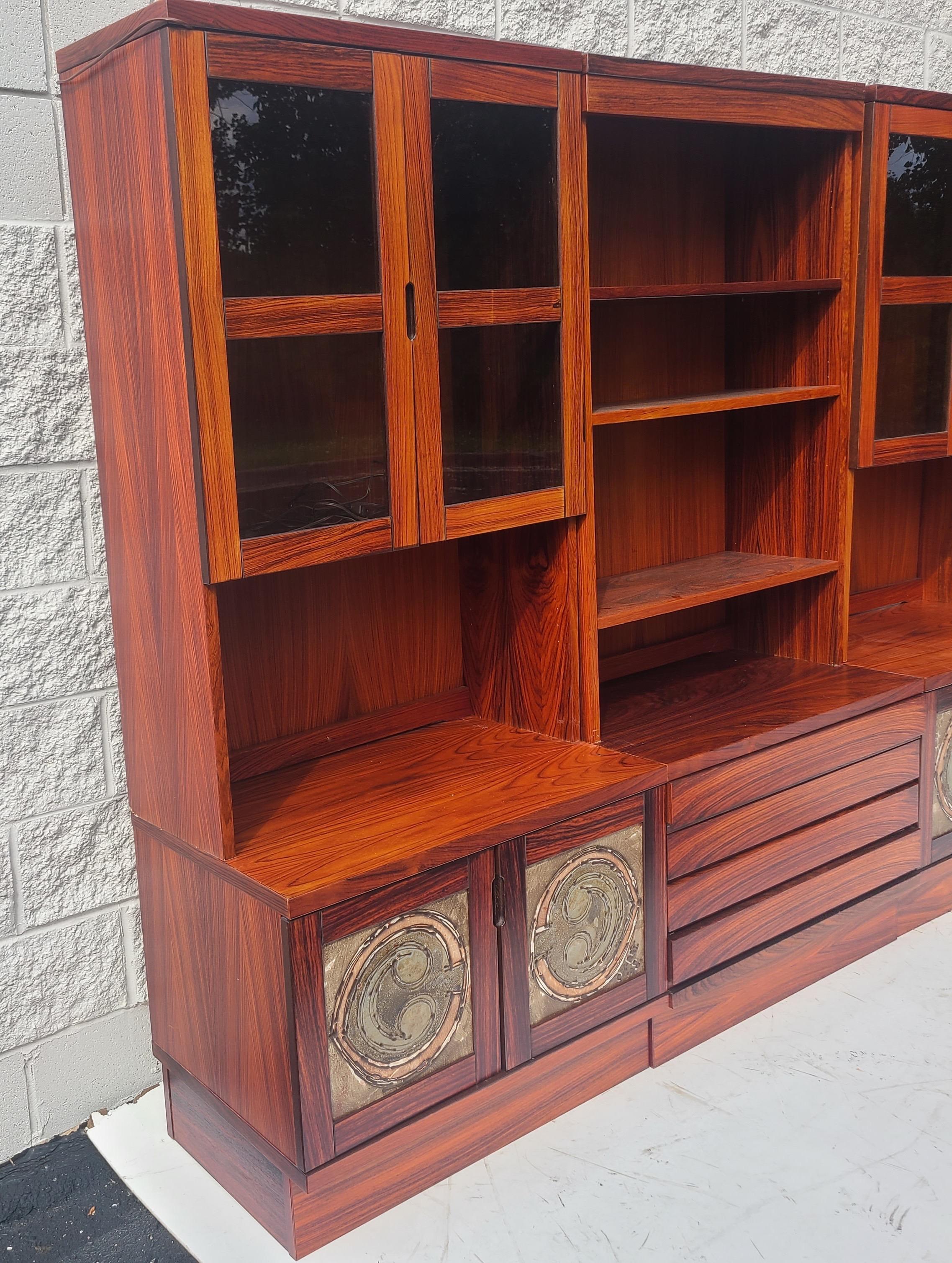 Rosewood Wall Unit. Made in Denmark. Has ceramic panels in lower
Doors which say Ox Art '78. Lower cabinets have mahogany shelved. 
Upper cabinets have a glass shelves behind glass doors. Center cabinet
Lower has drawers.

    