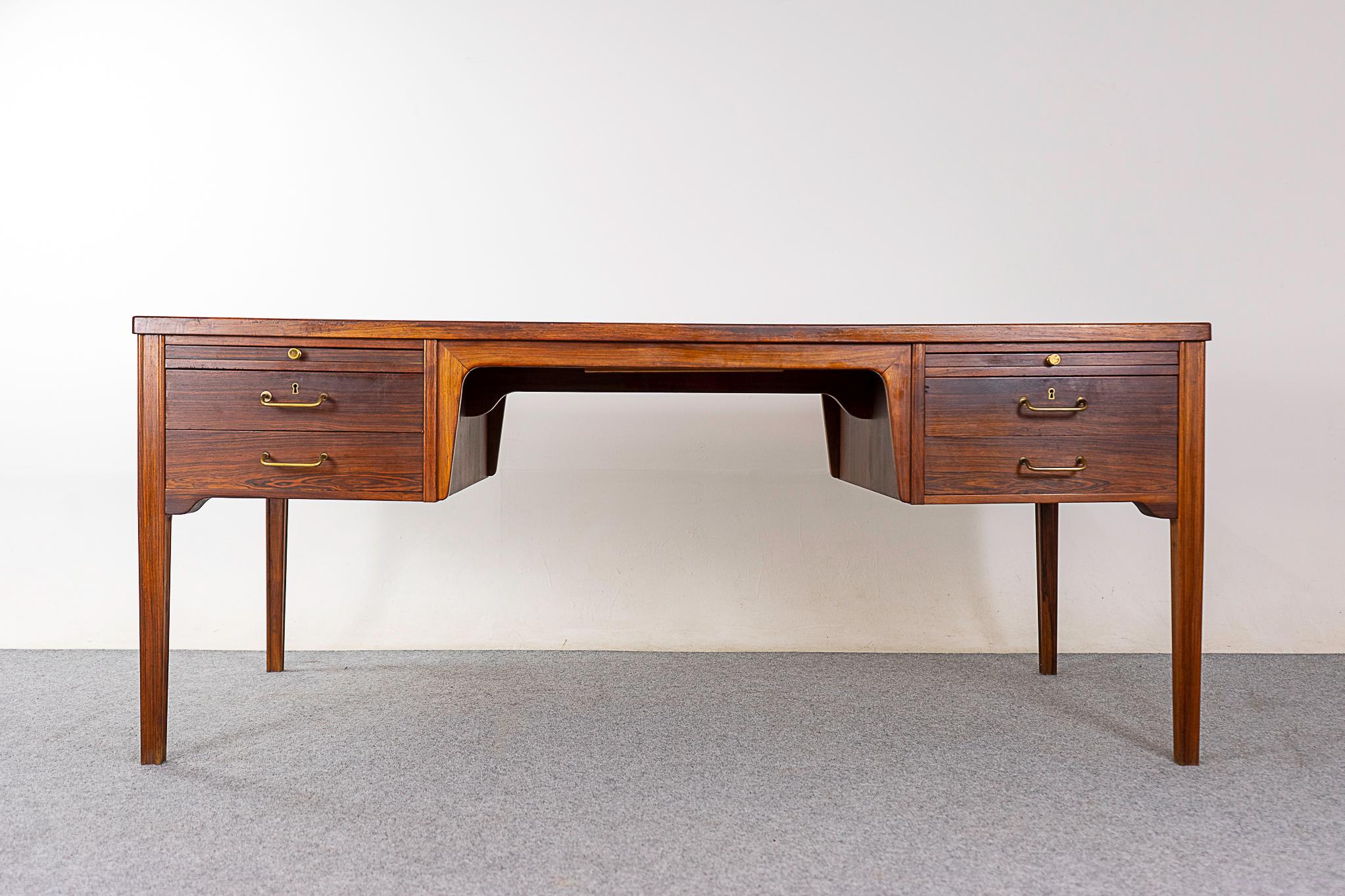 Rosewood mid-century desk, circa 1960's. Beautiful bookmatched veneer throughout, lovely brass details and lockable top drawers. Unique slide out back leaf adds extra surface area to the already generous top! Lovely arches in the knee opening. This