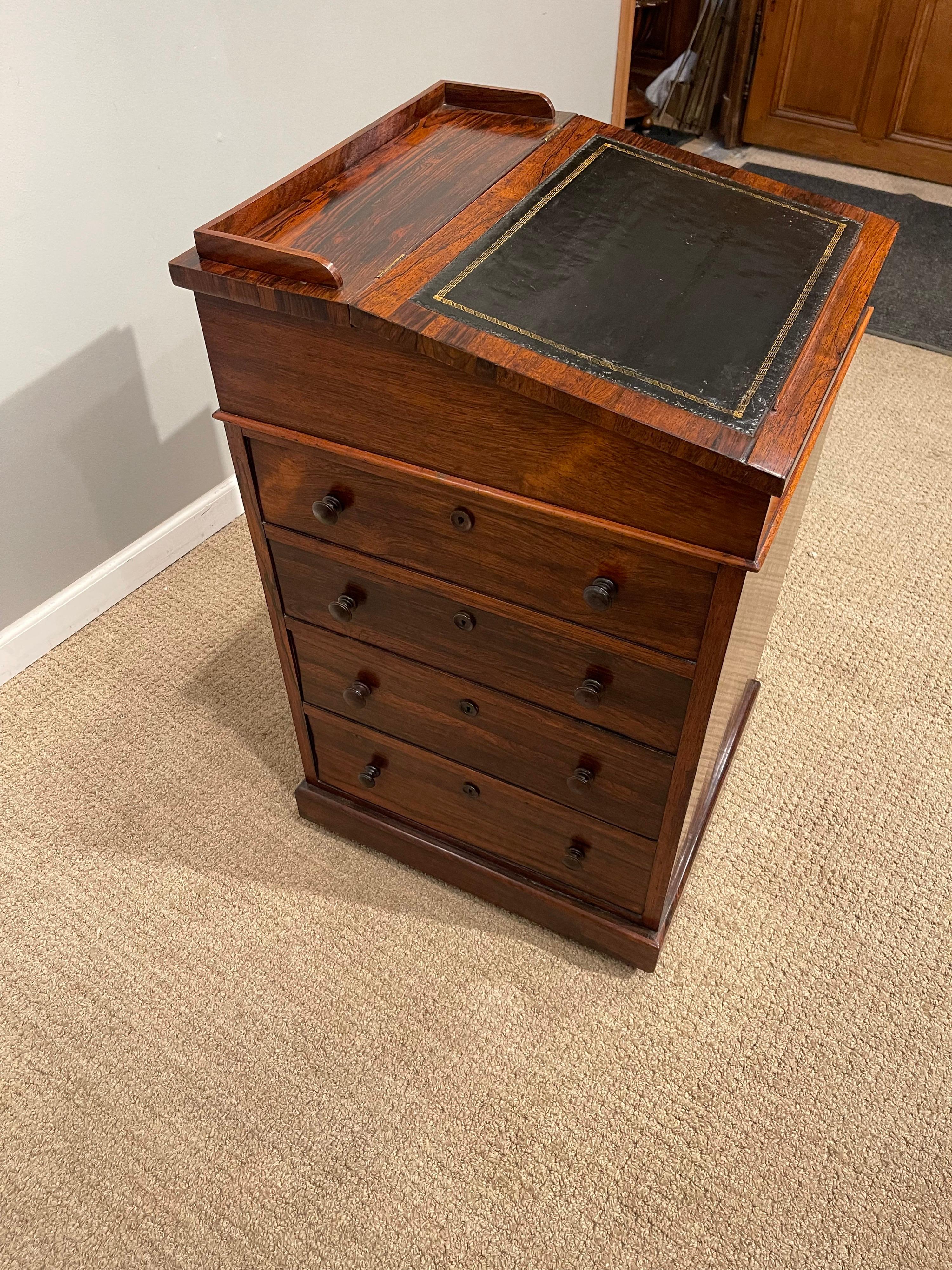 An early 19th century rosewood davenport desk, with low gallery above a lifting slant front
writing surface, with inset leather top & gold tooling. A small inkwell & pen holding & draw & pivoting drawer. It's interior having small drawers above 4