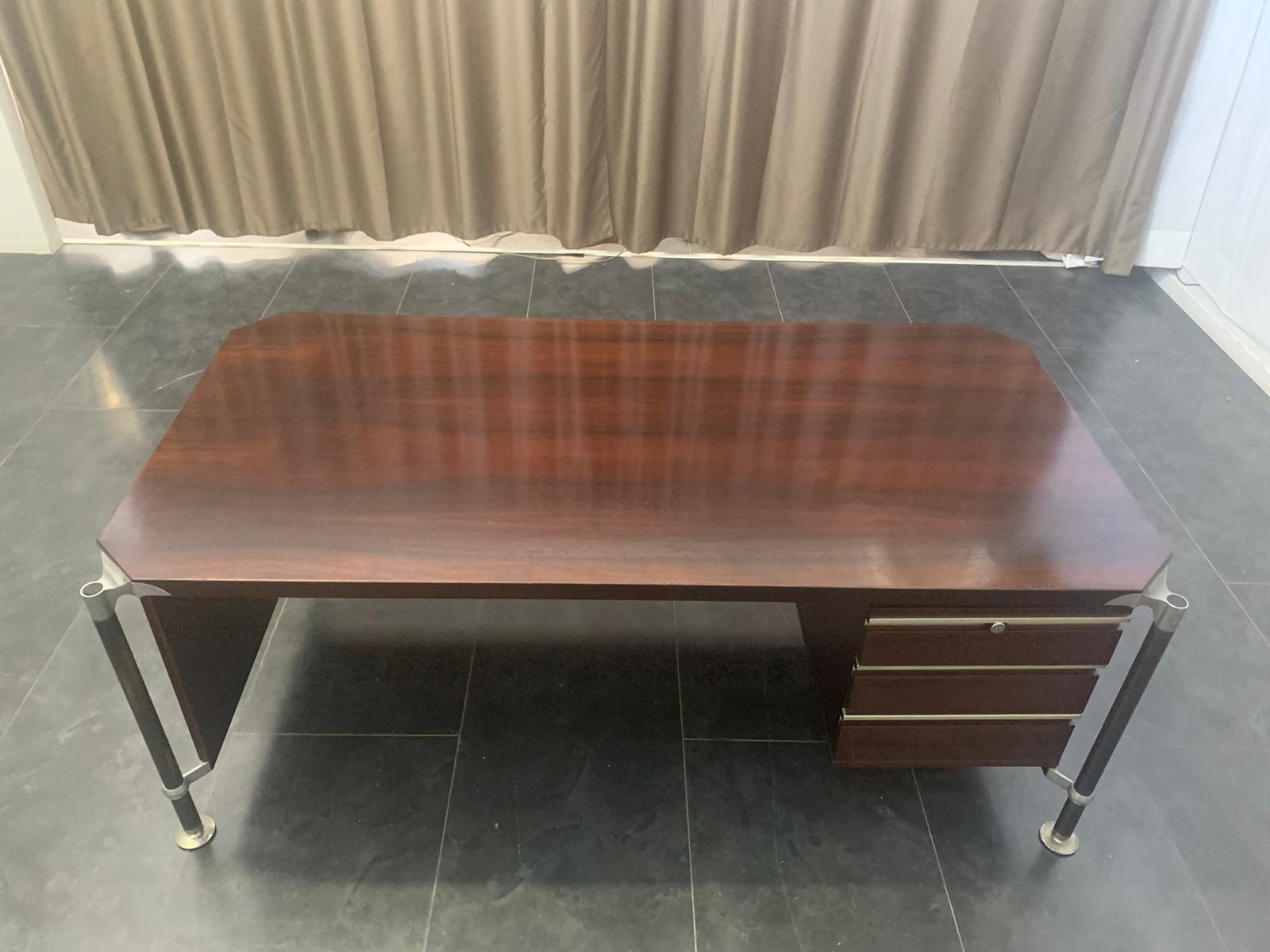 Executive desk in rosewood with top connected with polished aluminum corner fittings to the legs in black painted steel. The desk is solid is fully functional, the chest of drawers and there is a lock the key is missing. The rosewood with flame