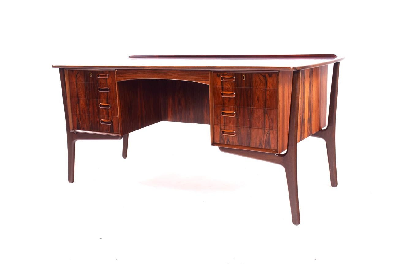 This elegant rosewood desk by Svend Aage Madsen for Sigurd Hansen, features a unique floating frame design with wonderful sculpted legs and curved tabletop. High quality and great details. Eight drawers and an additional cabinet space on the back