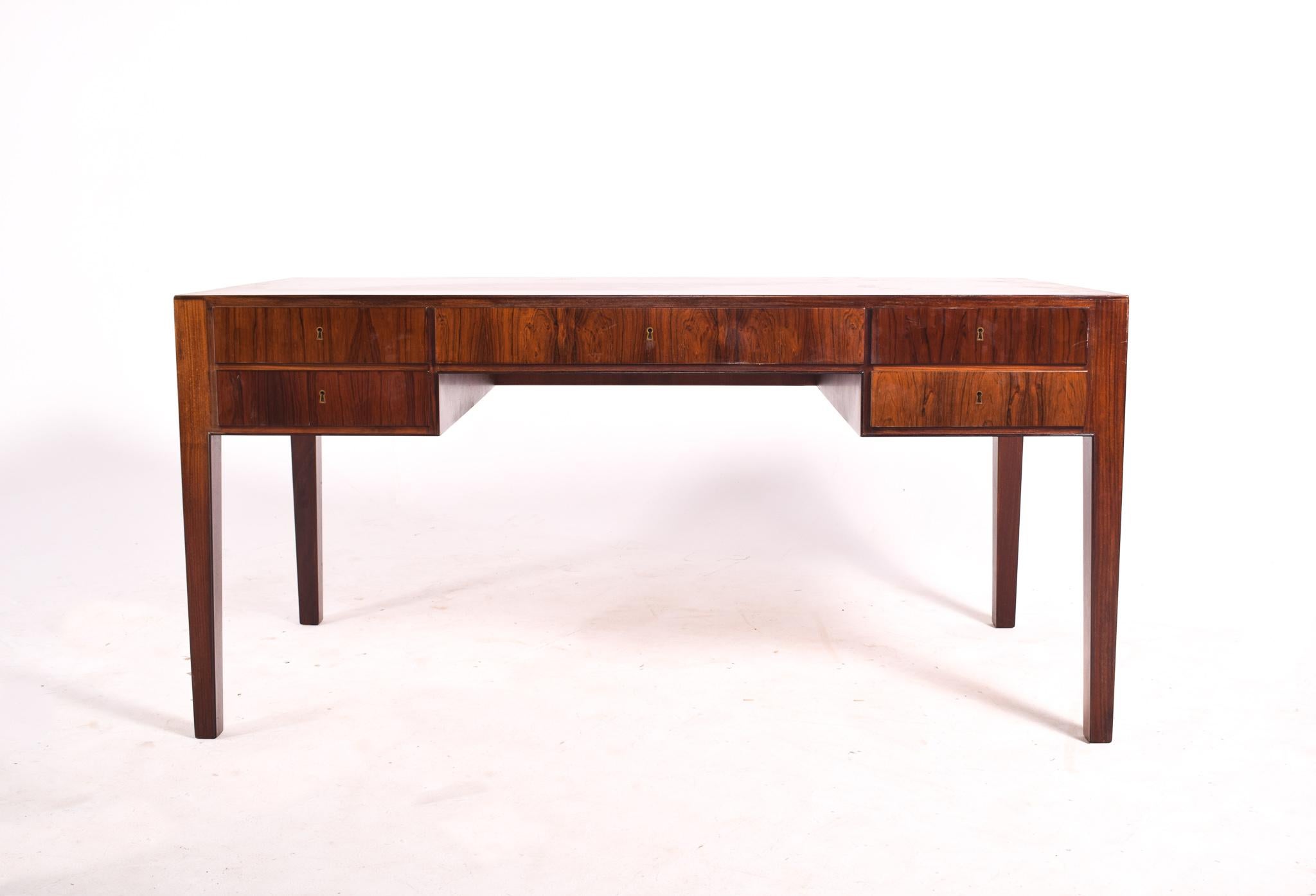 Very elegant writing desk by Ole Wanscher, 1950. This rosewood veneer writing desk is very nice with typical Danish refined details all over. This rosewood desk was manufactured by A.J. Iversen during the 1950s. It has five elegant drawers plus a