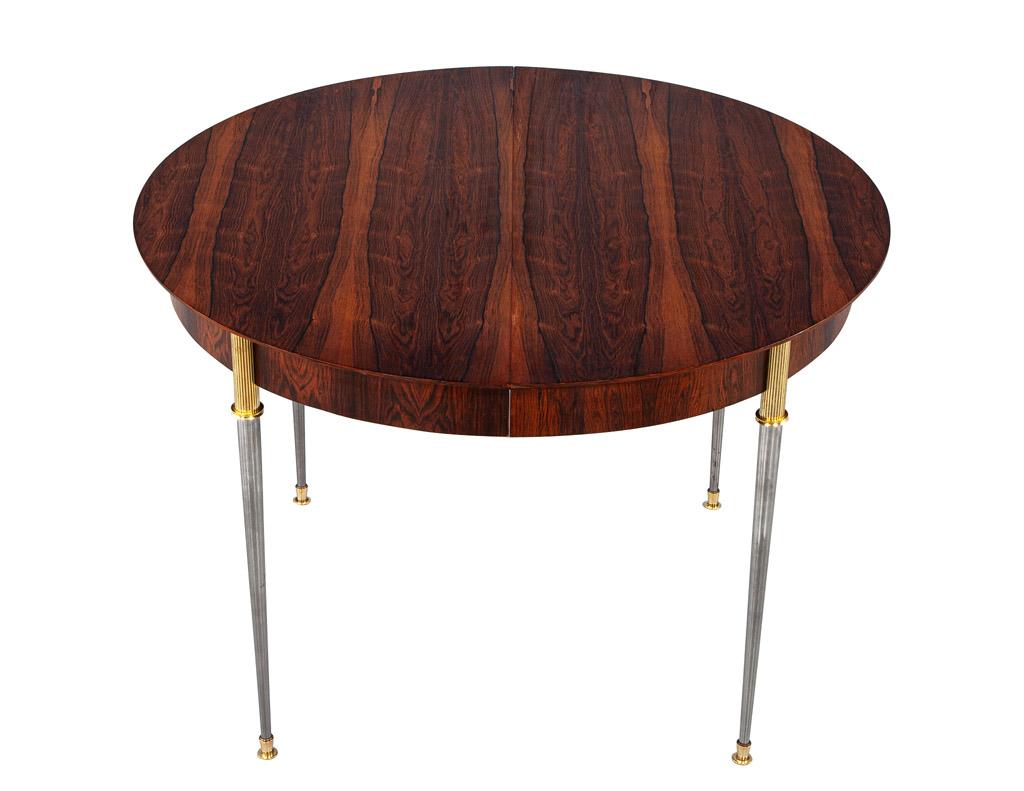 This is an original art deco rosewood dining table by iconic designer Jules Leleu, made in France, circa 1950s. This exquisite table features stainless steel legs with beautiful bronze ornaments. The table closed is 43” in diameter and opens to a