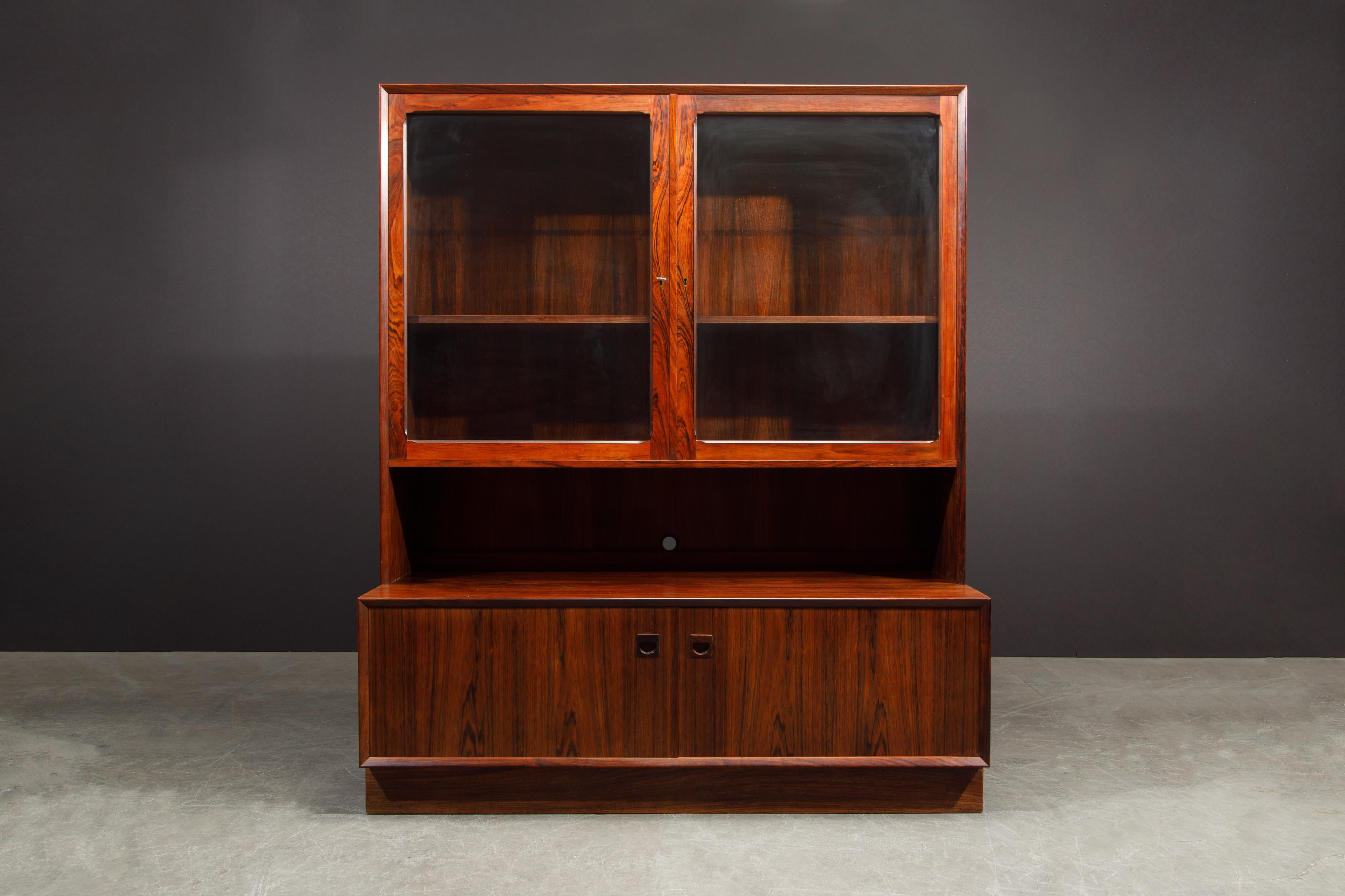 A beautiful 1960s Mid-Century Modern vitrine in rosewood that possesses incredible grain detail by Eric Brouer for Brouer Møbelfabrik, Denmark. A glass display china cabinet sits atop a rosewood credenza and within the two glass doors are two wood