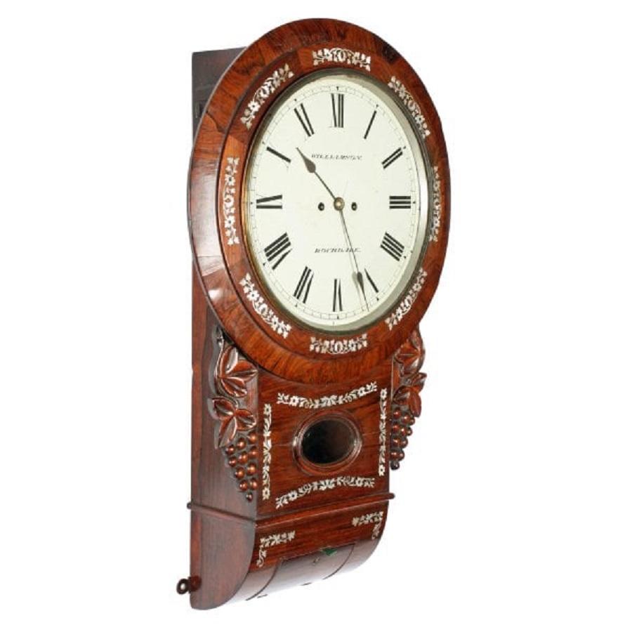 A middle of the 19th century rosewood cased wall clock.

The clock has an eight day, double fusee works that strike the hour on a bell.

The rosewood drop case has carved decoration of vine leaves and grapes and is inlaid with mother of