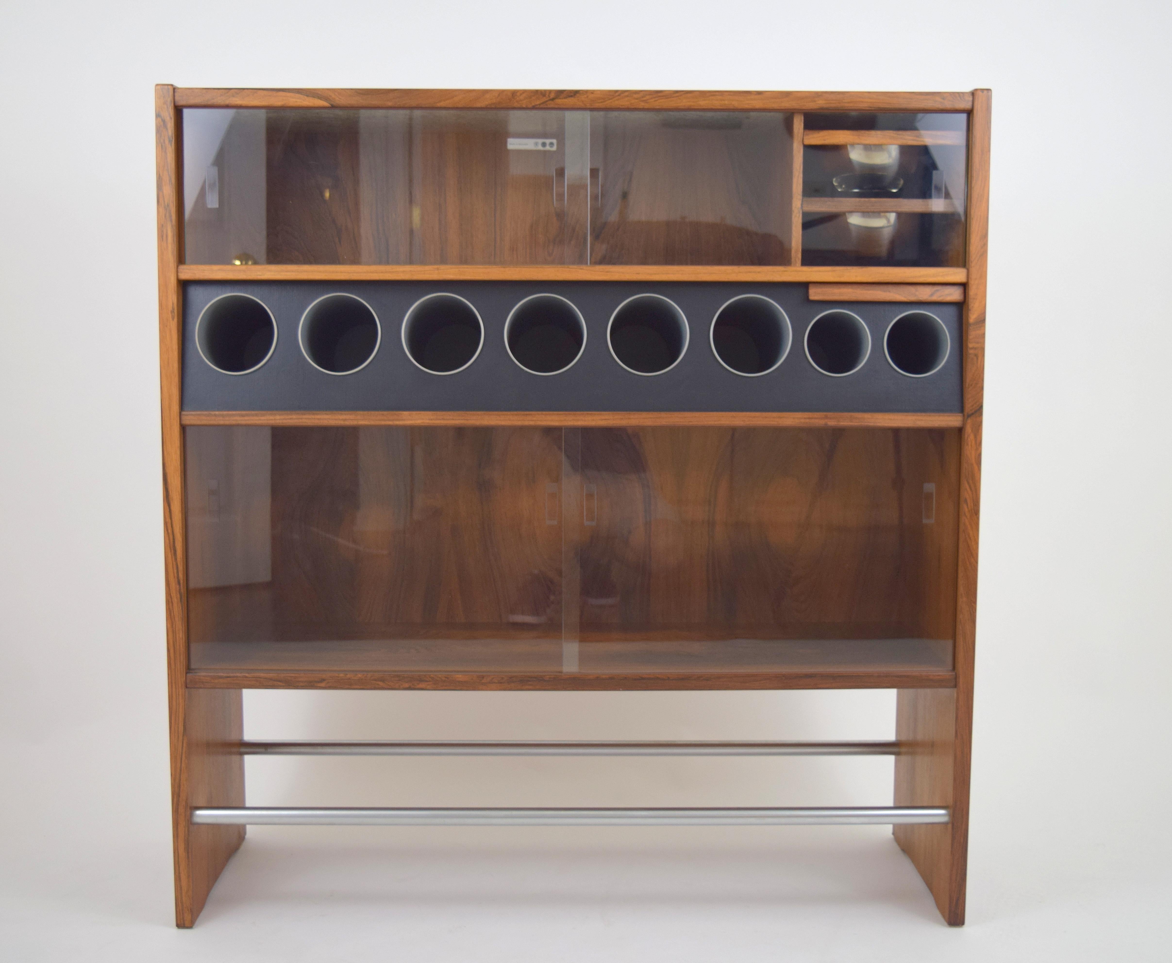 Highly functional rosewood dry bar by Erik Buch. Beautifully grained rosewood case with varying sized bottle storage tubes, two pull-out removable stainless steel bowls, pull-out tray, Two stainless steel foot rest bars, and two open storage areas