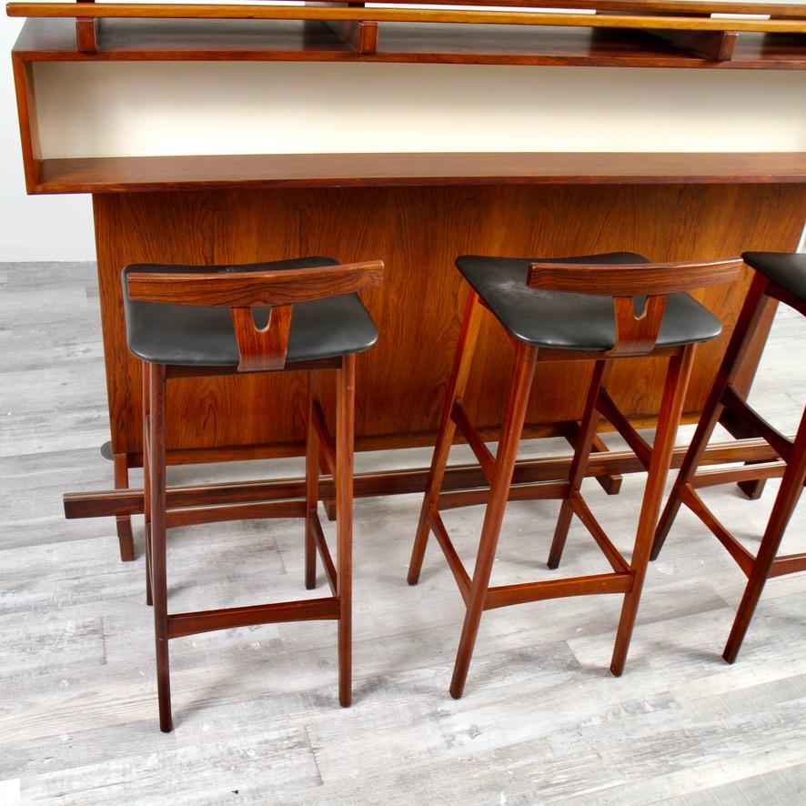 Erik Buch for Dyrlund dry bar and three matching rosewood stools. Stunning Scandinavian Modern dry bar from the1960s. This piece is completely executed in rosewood veneer, that shows the front side of the bar has shelf and a long rosewood and metal