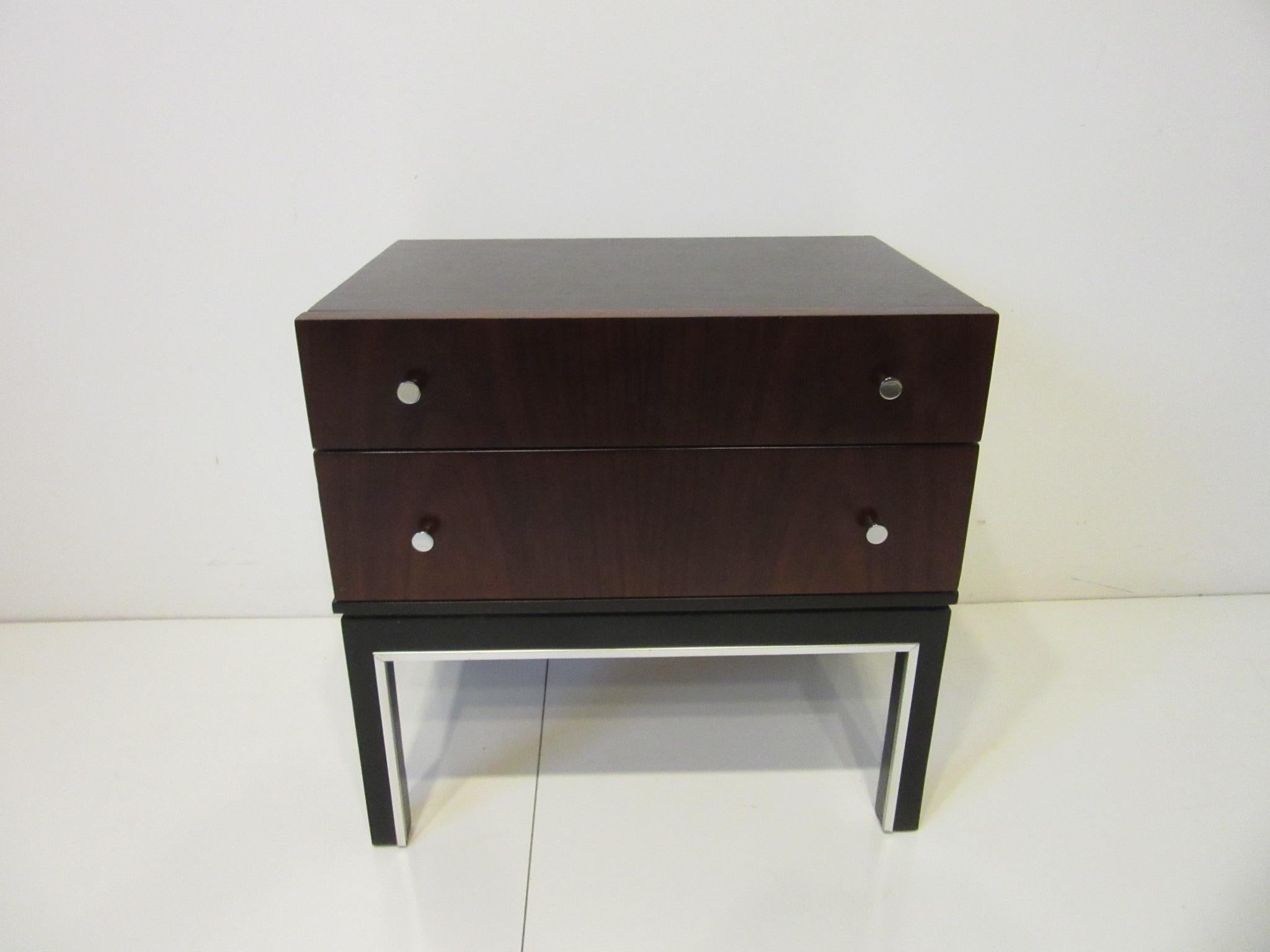 A rosewood and ebony toned two drawer nightstand / end table with chrome pulls having aluminum trim to the lower stretcher and leg area. A very tight and crisp looking design retaining the manufactures branded mark by the American of Martinsville