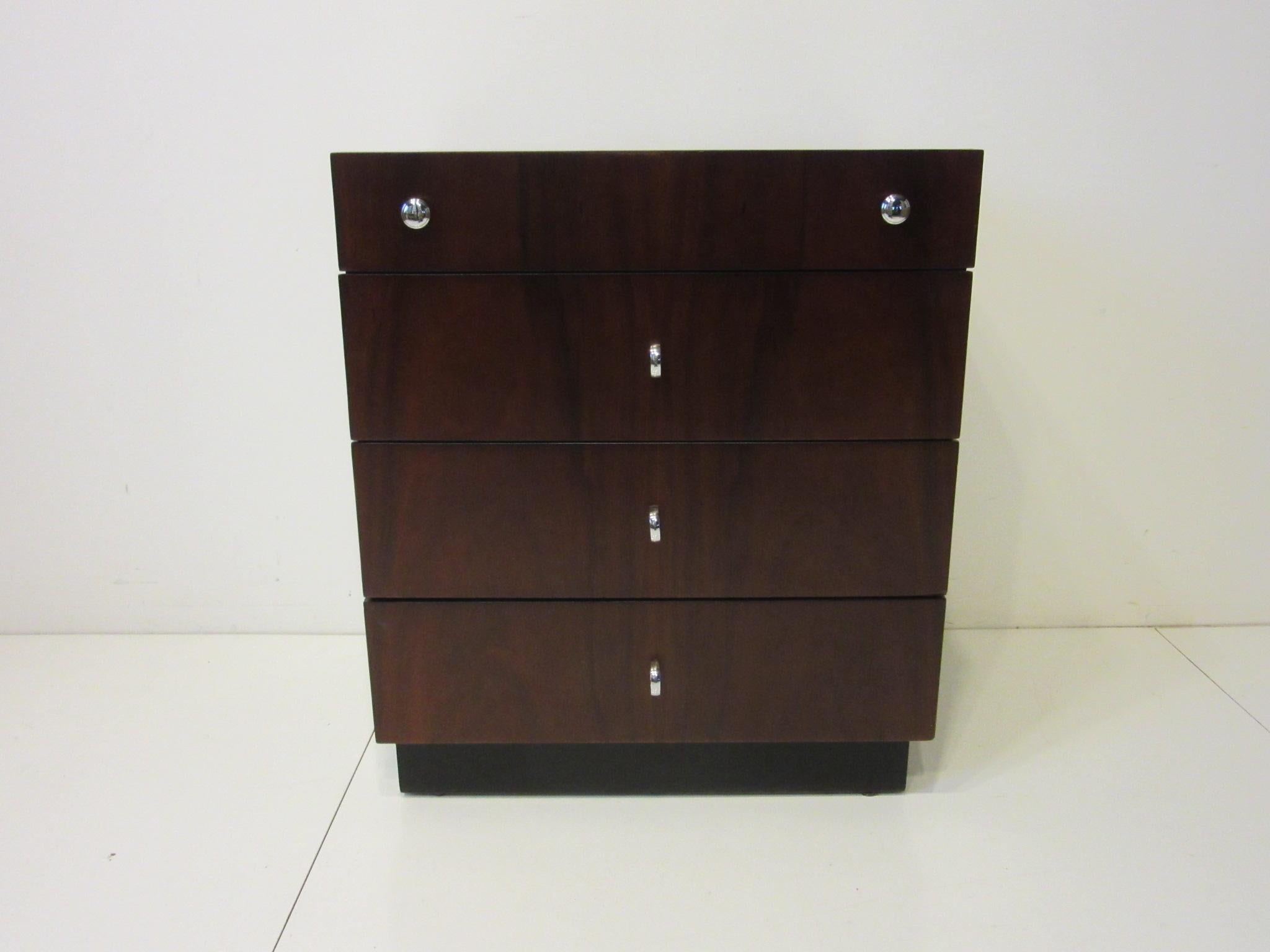 A four drawer rosewood and ebony toned small chest or nightstand having rich graining with chrome pulls . A great chest for a tight space or use as a nightstand because of it's taller profile to match todays pillow top styled beds , retains the