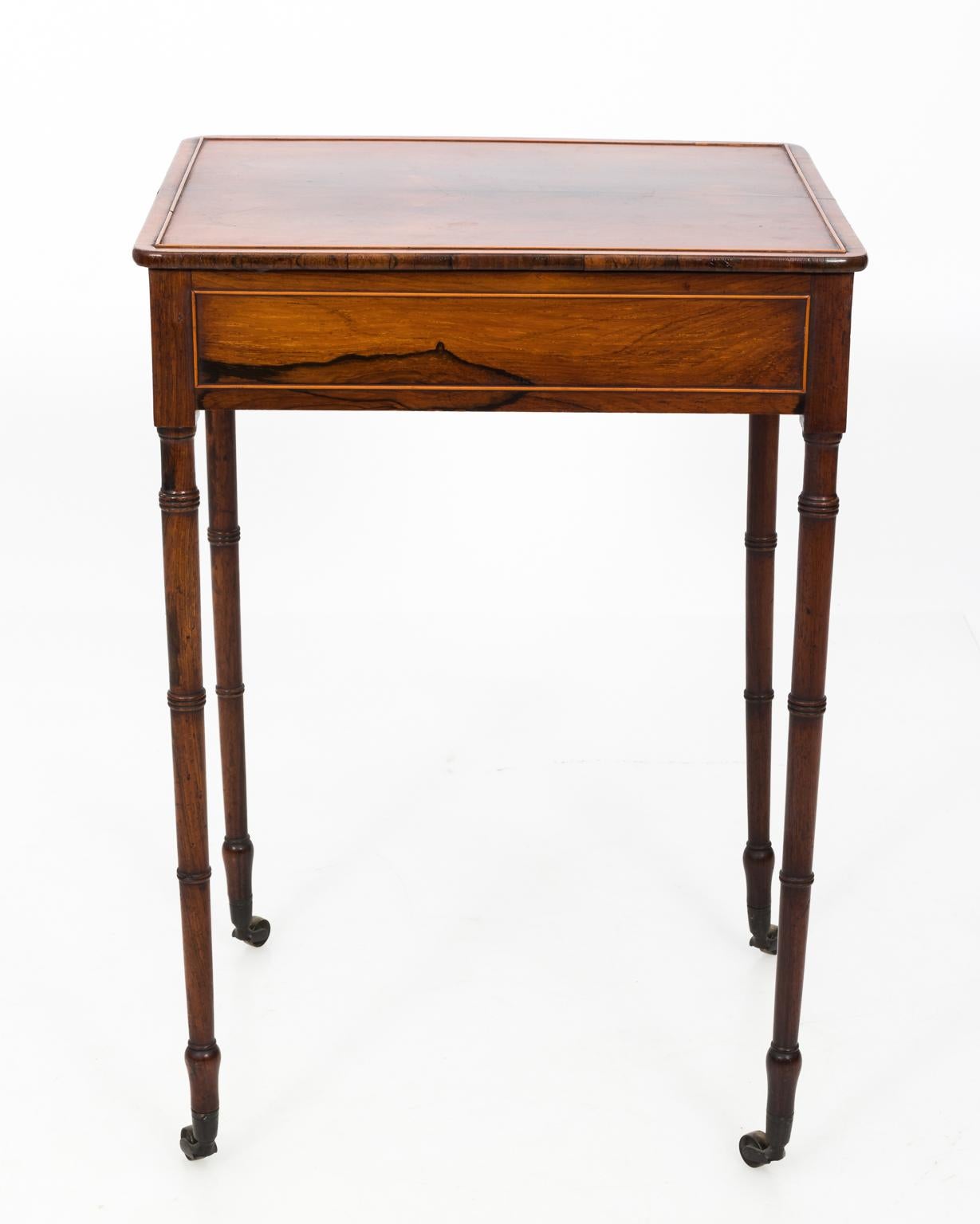 Rosewood English Regency writing table with one hidden drawer on castors, circa 19th century. The table also features raised wood inlay trim and faux-bamboo turned legs.