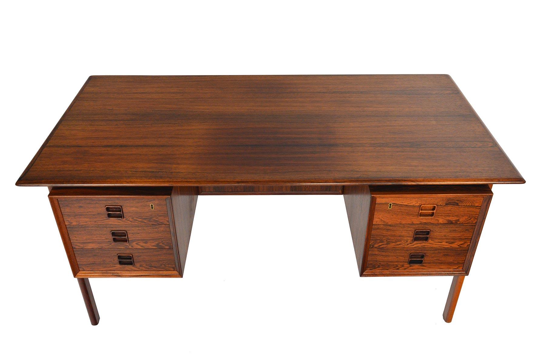 This handsome Brazilian rosewood executive desk was designed by Arne Vodder in the 1960s. Two banks of three drawers flank a spacious kneehole. Sculpted exterior mounted legs create visual interest and support the desk surface. The back of this desk