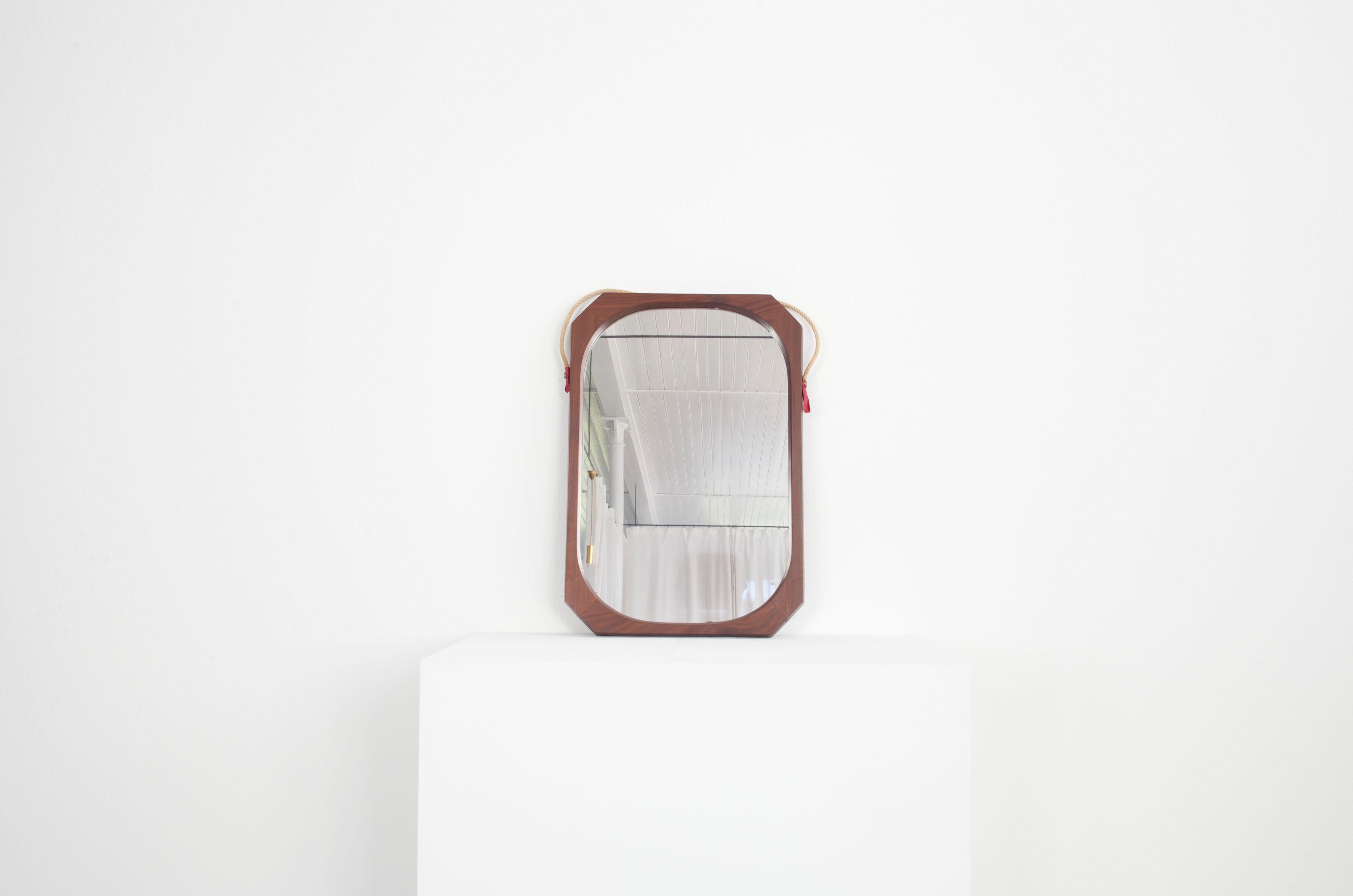 Ce miroir italien date des années 60. Le cadre en bois a une forme particulière : alors que les bords extérieurs sont anguleux, le cadre est rond à l'intérieur. Le miroir est également muni d'une corde qui permet de l'attacher à un mur. La corde est