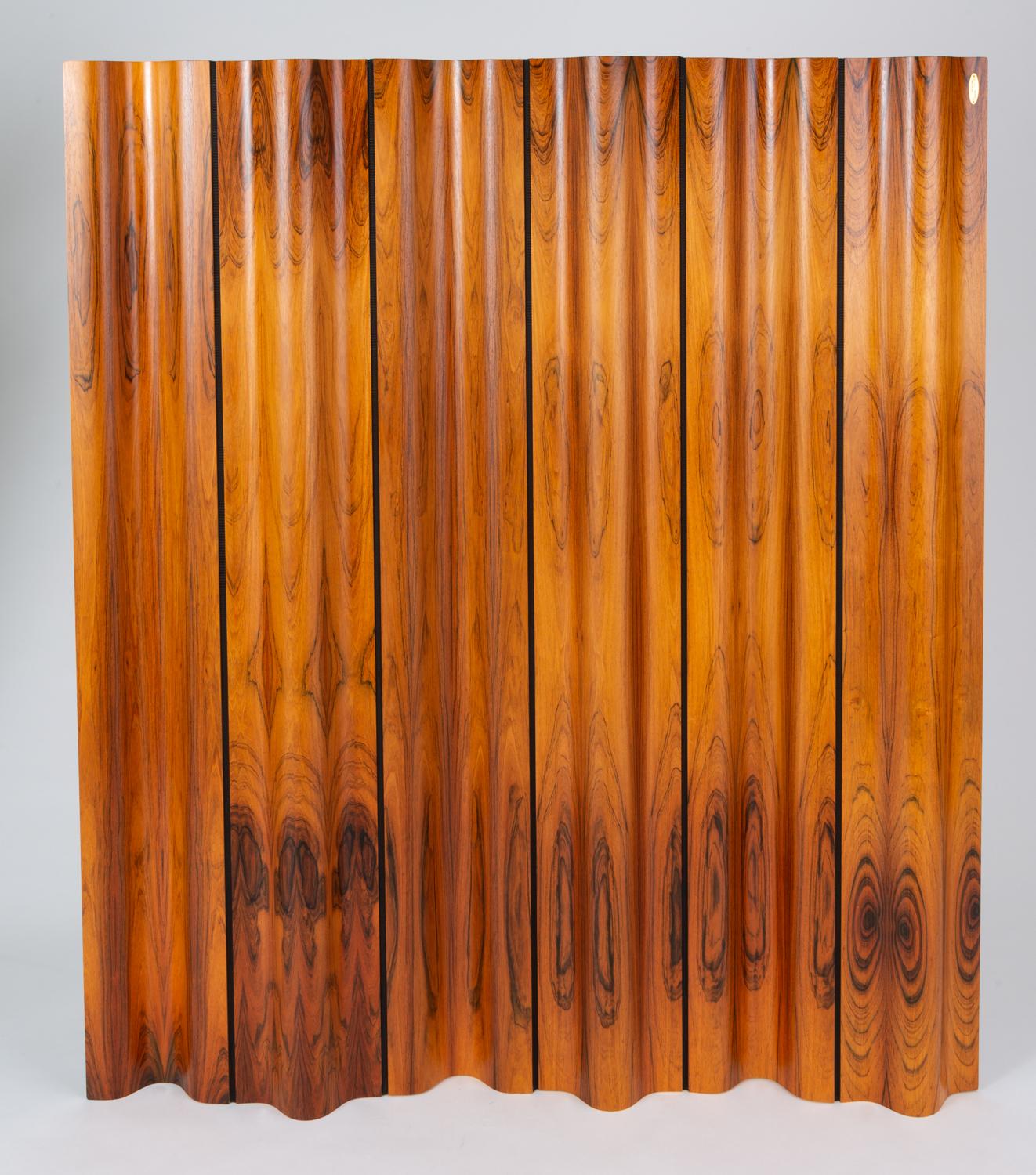 Ray and Charles Eames’ iconic folding screen for Herman Miller, seen here in rosewood. The undulating design is composed of articulated panels of curved rosewood, joined by a supple brown fabric, for a high level of flexibility in positioning.