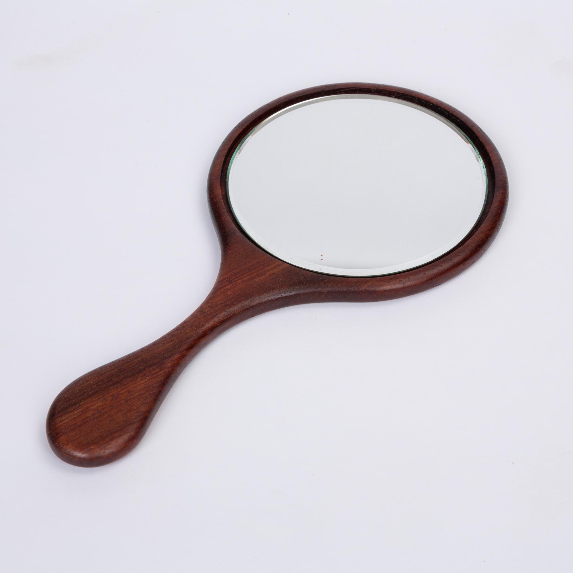 Vintage rosewood hand mirror with hand carved organic shaped handle. The mirror features a highly figured rosewood handle and frame, with a 5” piece of mirror glass inset into the frame. There is a small border separating the glass from the frame